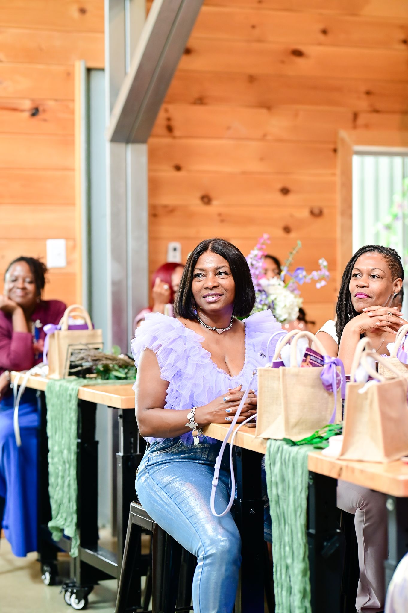 Women seated at wooden tables with gift bags at an indoor event in a rustic wood-paneled venue.