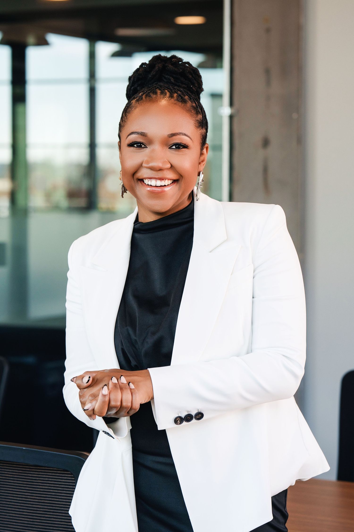 Professional portrait of a businesswoman in a crisp white blazer and black top smiling warmly in an office setting.