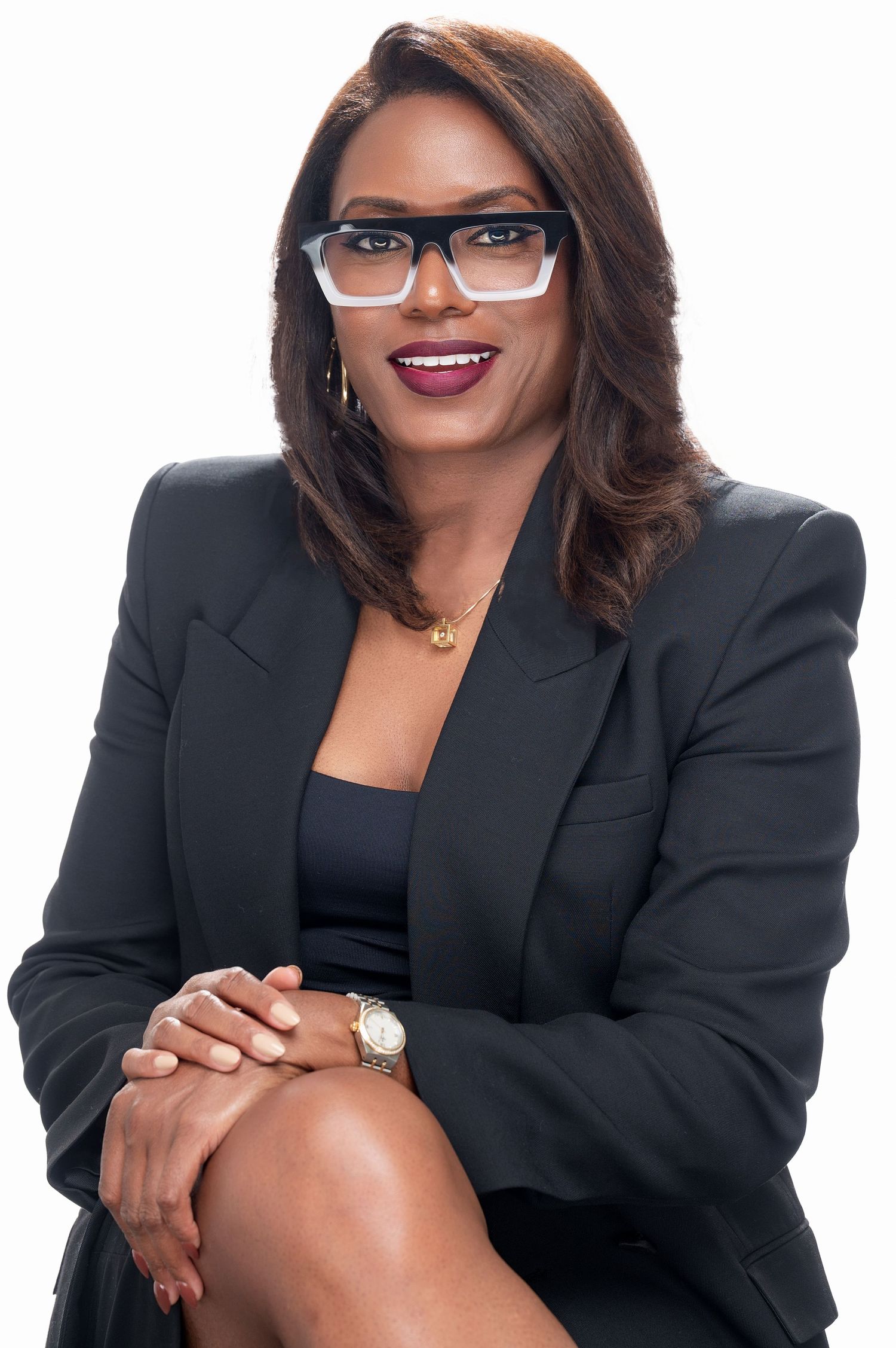 Professional business portrait of a smiling woman wearing glasses and a black blazer sitting against white background.