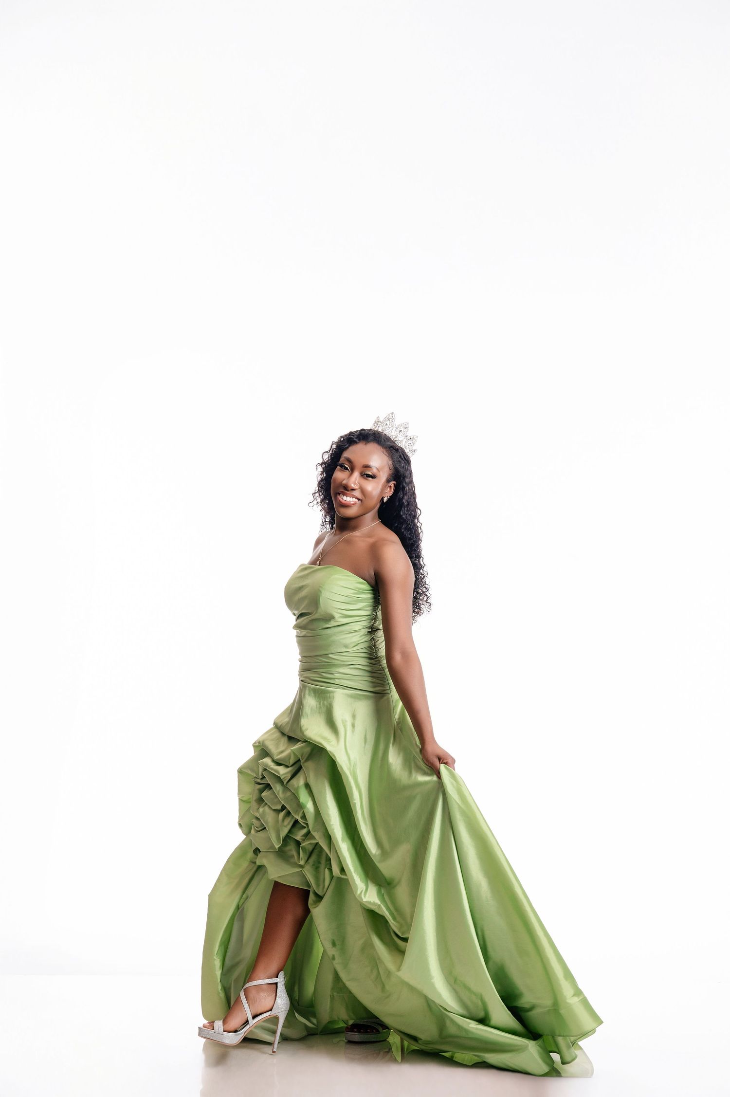 Someone wearing a strapless light green evening gown with ruffled details poses elegantly against a white background.