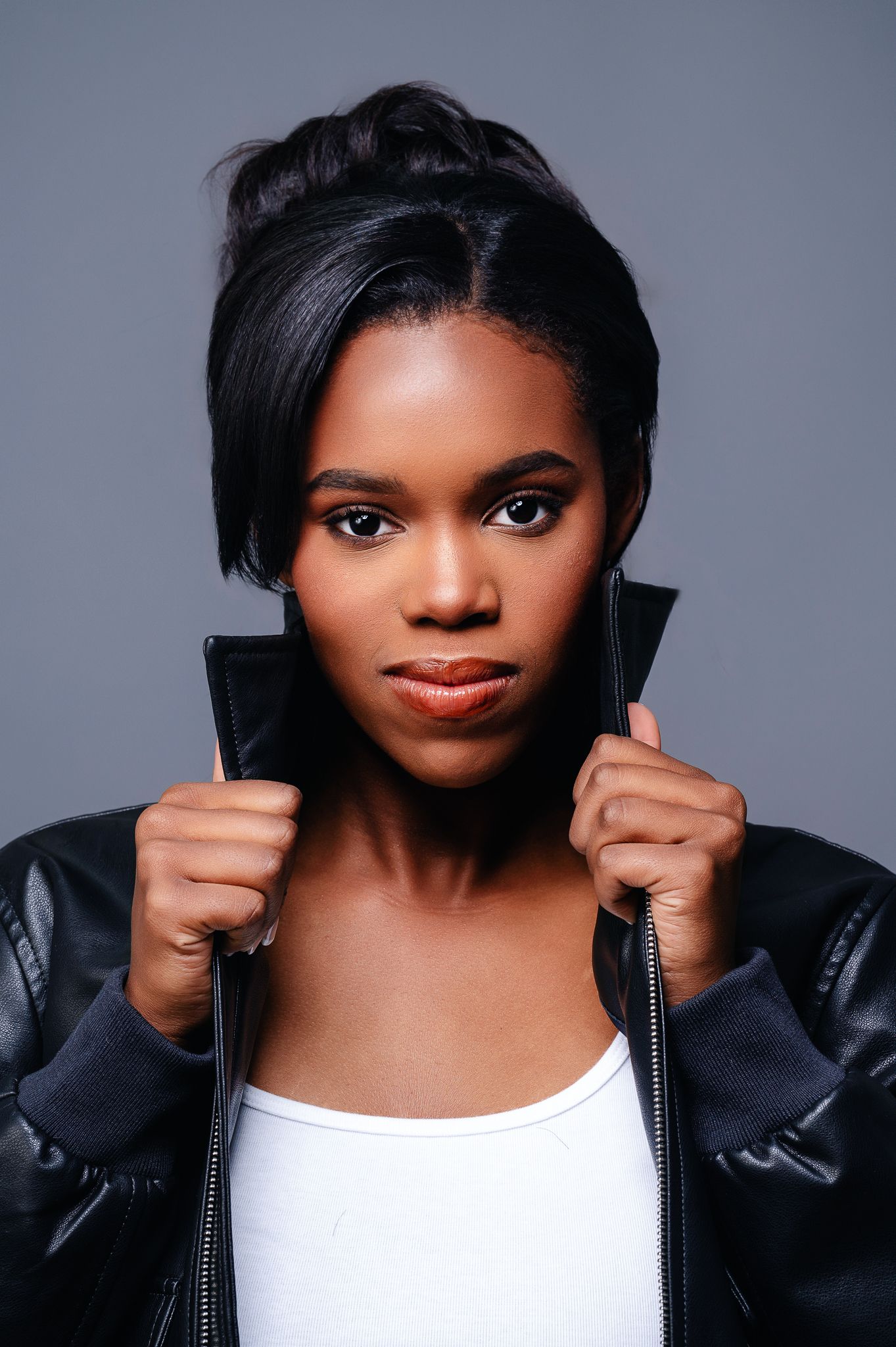 Studio portrait in black leather jacket and white top against gray background.