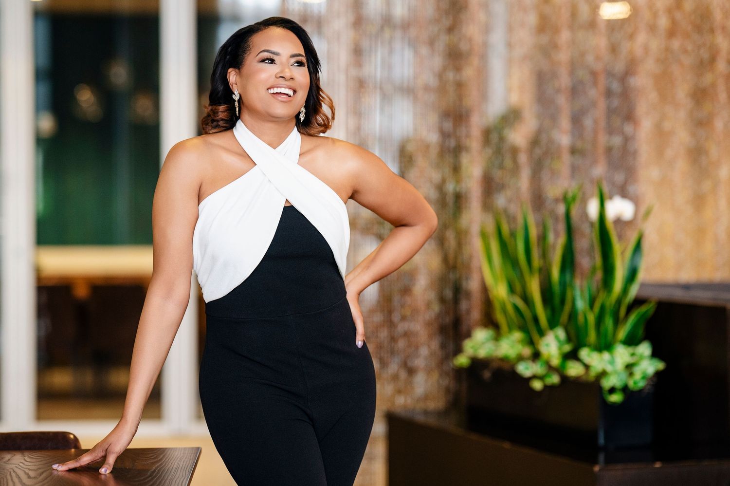 A black and white halter evening dress is worn by someone posing elegantly against a modern interior backdrop.