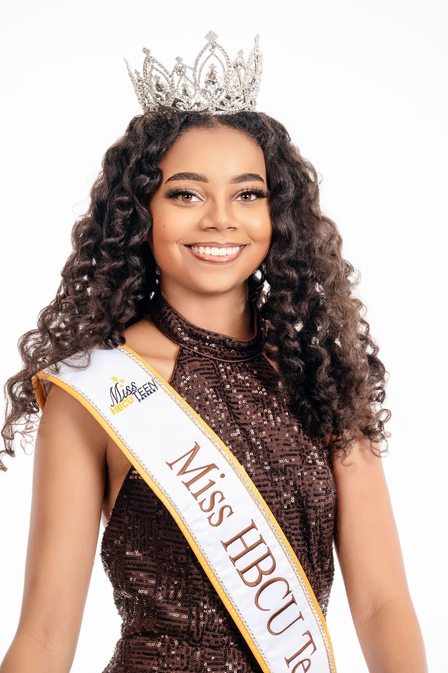 A pageant contestant wearing a sparkling brown dress, crown, and Miss HBCU sash smiles against a white background.