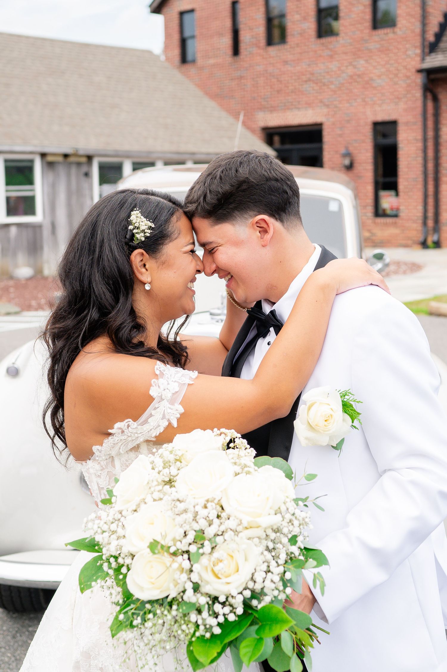 A romantic wedding moment with a white rose bouquet and the wedding couple sharing a tender embrace outdoors.