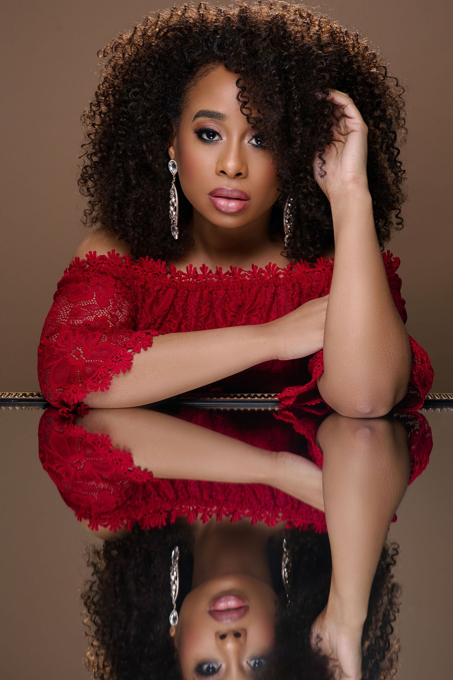 Fashion portrait featuring a deep red textured dress and natural curly hair against a brown backdrop.