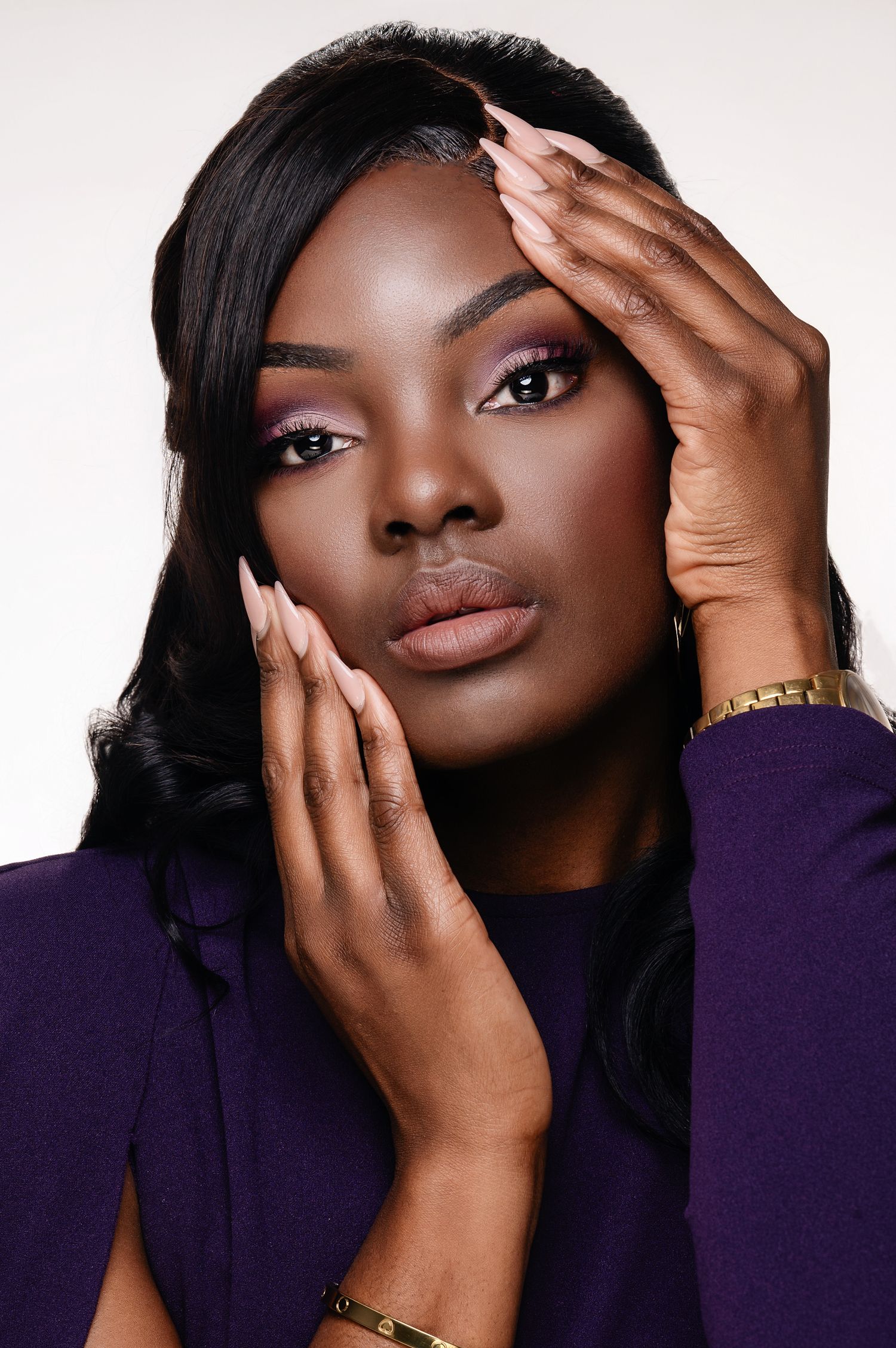 Beauty portrait with purple sweater, long black hair, pink eyeshadow, long manicured nails and gold jewelry.