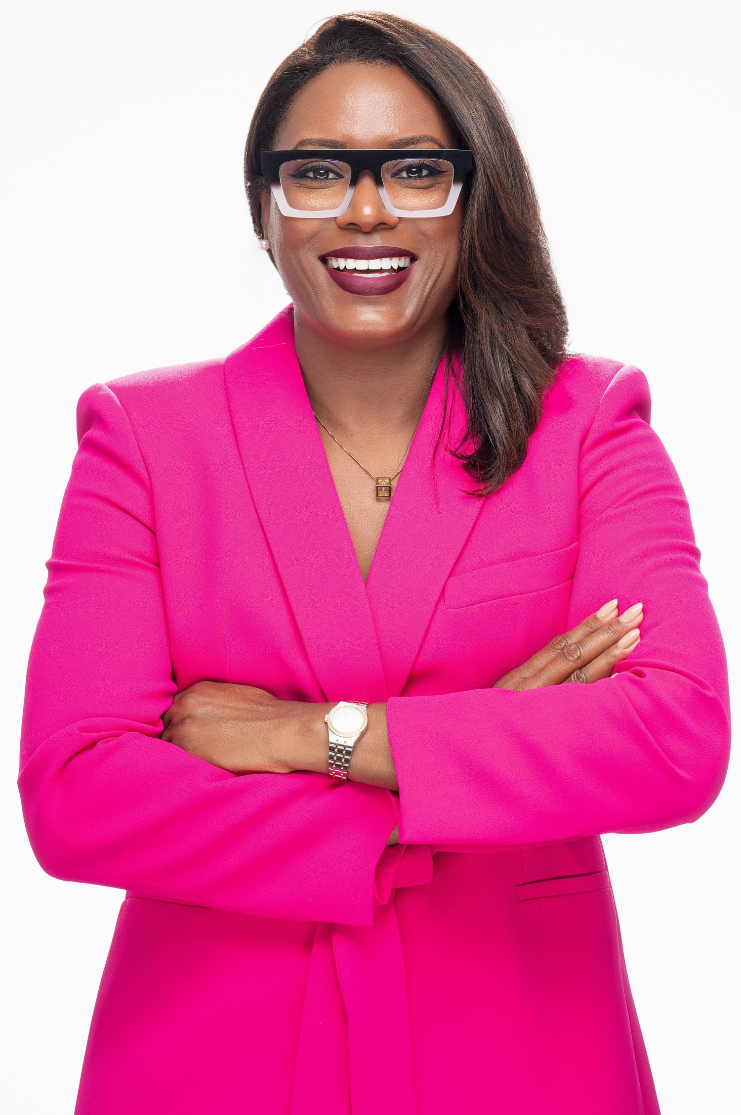 A professional wearing glasses and a bright pink blazer poses with crossed arms and a confident smile.