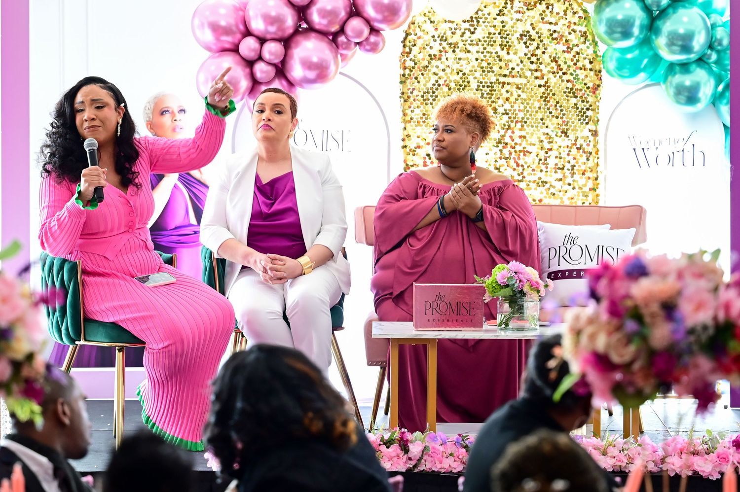Lively panel discussion event with colorful balloon decor and floral arrangements on stage against sparkly backdrop.