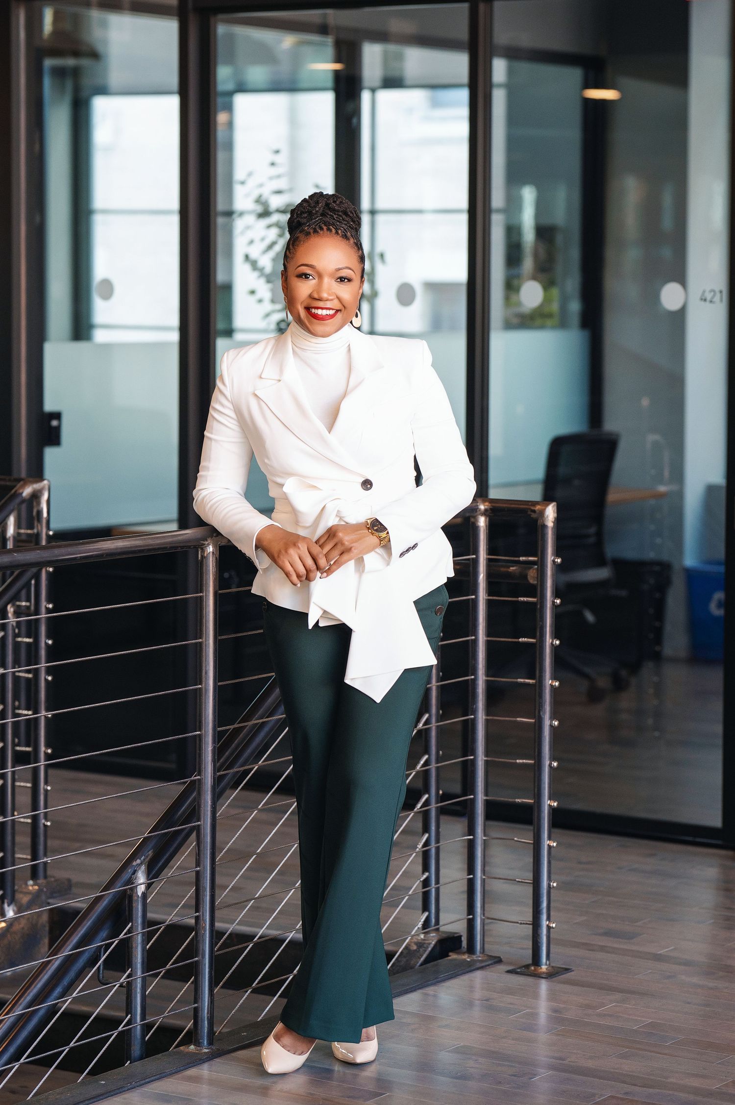 Professional in crisp white blazer and dark pants standing confidently in modern office setting.