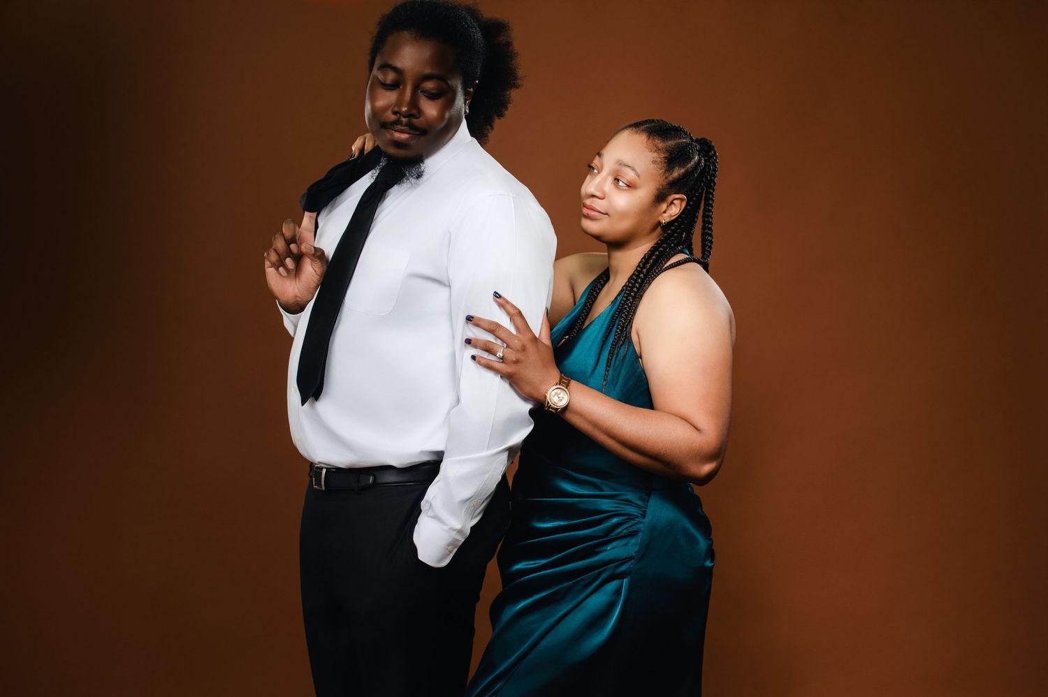 A couple in formal attire dances together in an intimate pose against a dark brown background.