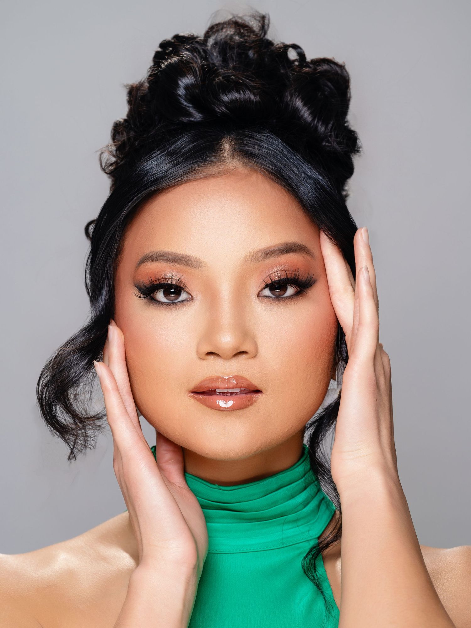 Beauty portrait featuring an elegant updo hairstyle and emerald green high neck top against a gray backdrop.