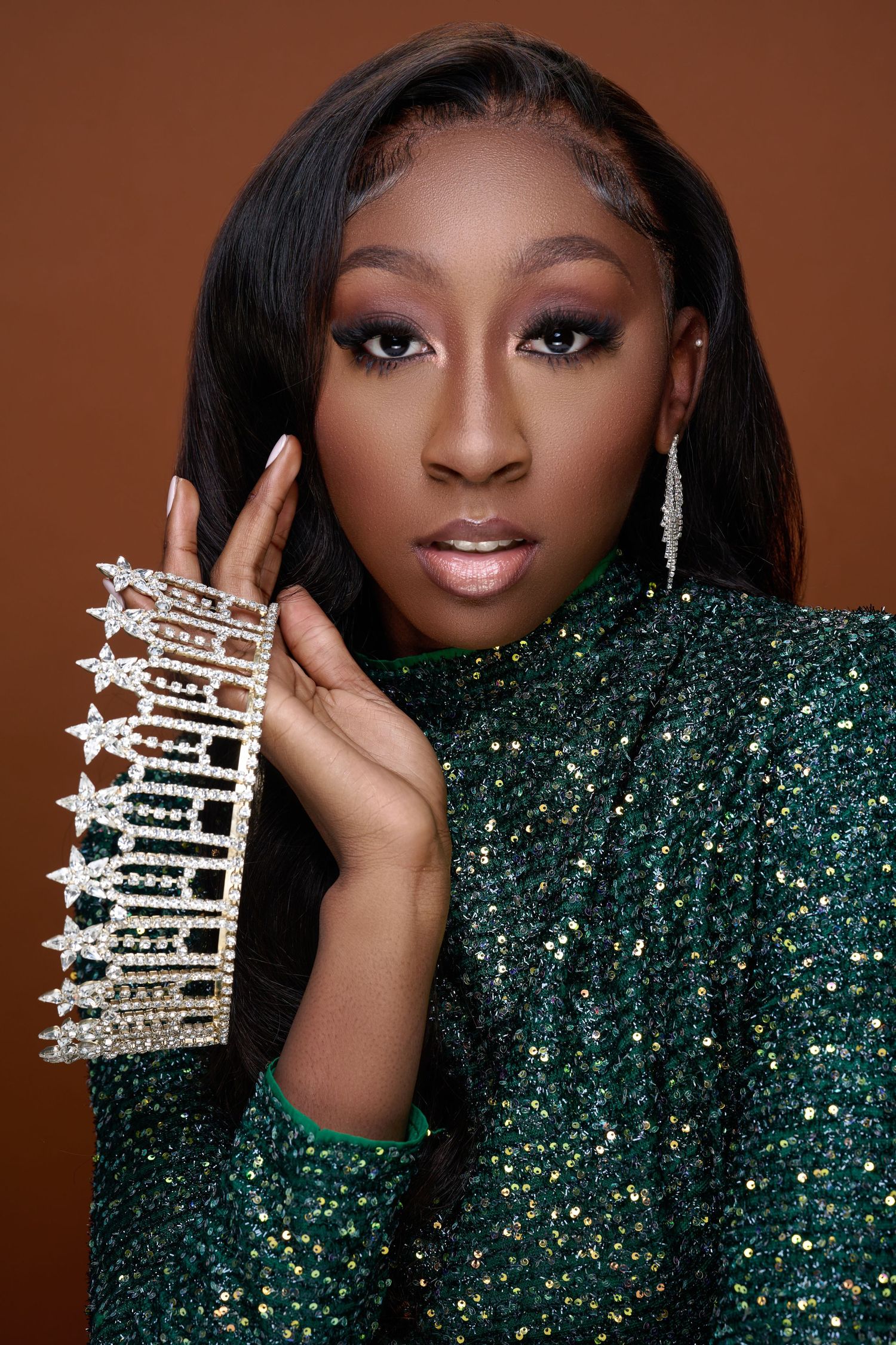 Glamorous portrait series showing sparkly emerald green sequin gown and crystal crown accessories against brown backdrop.