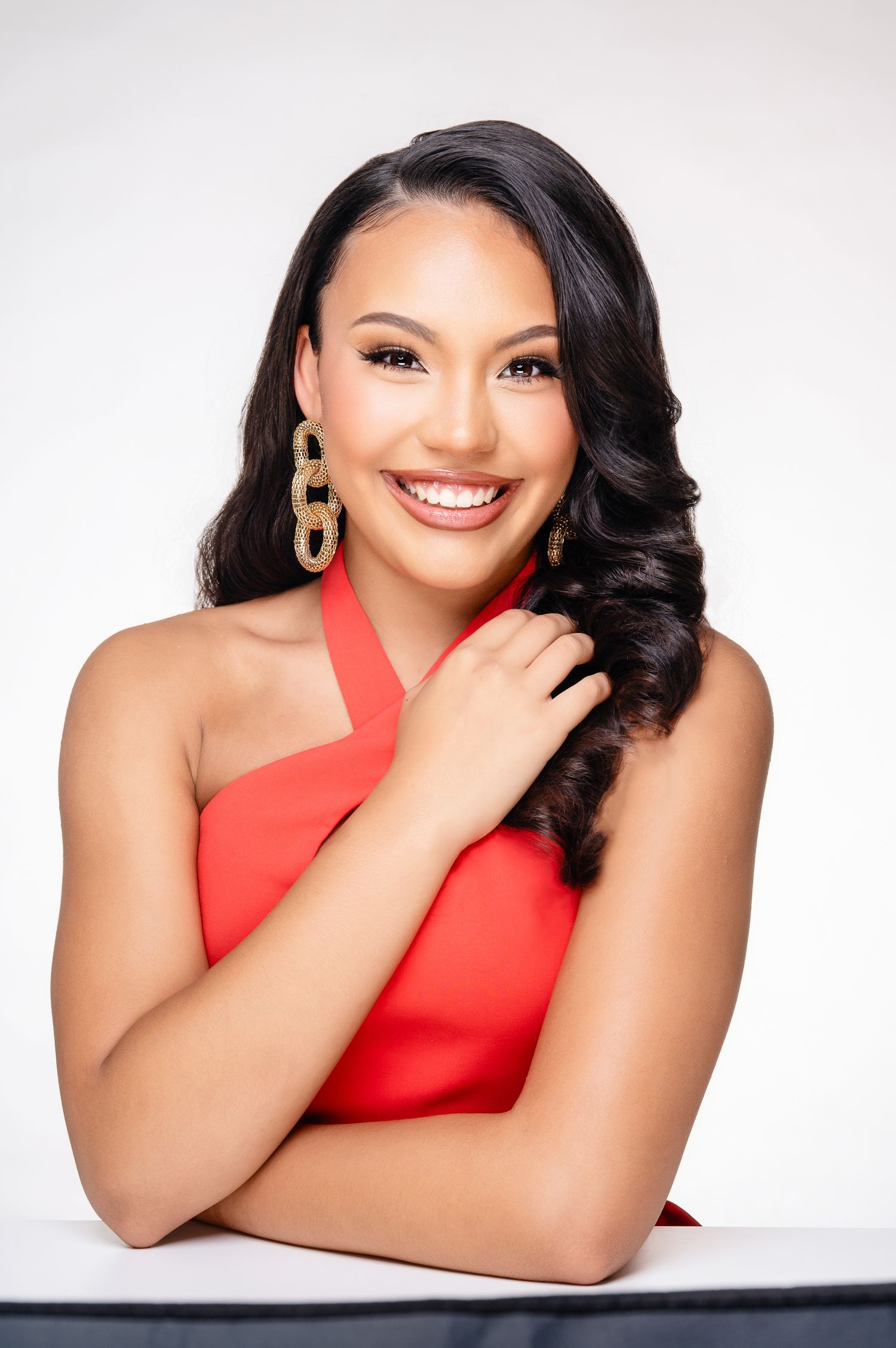 Woman in red sleeveless top poses elegantly against white background in professional portrait series.