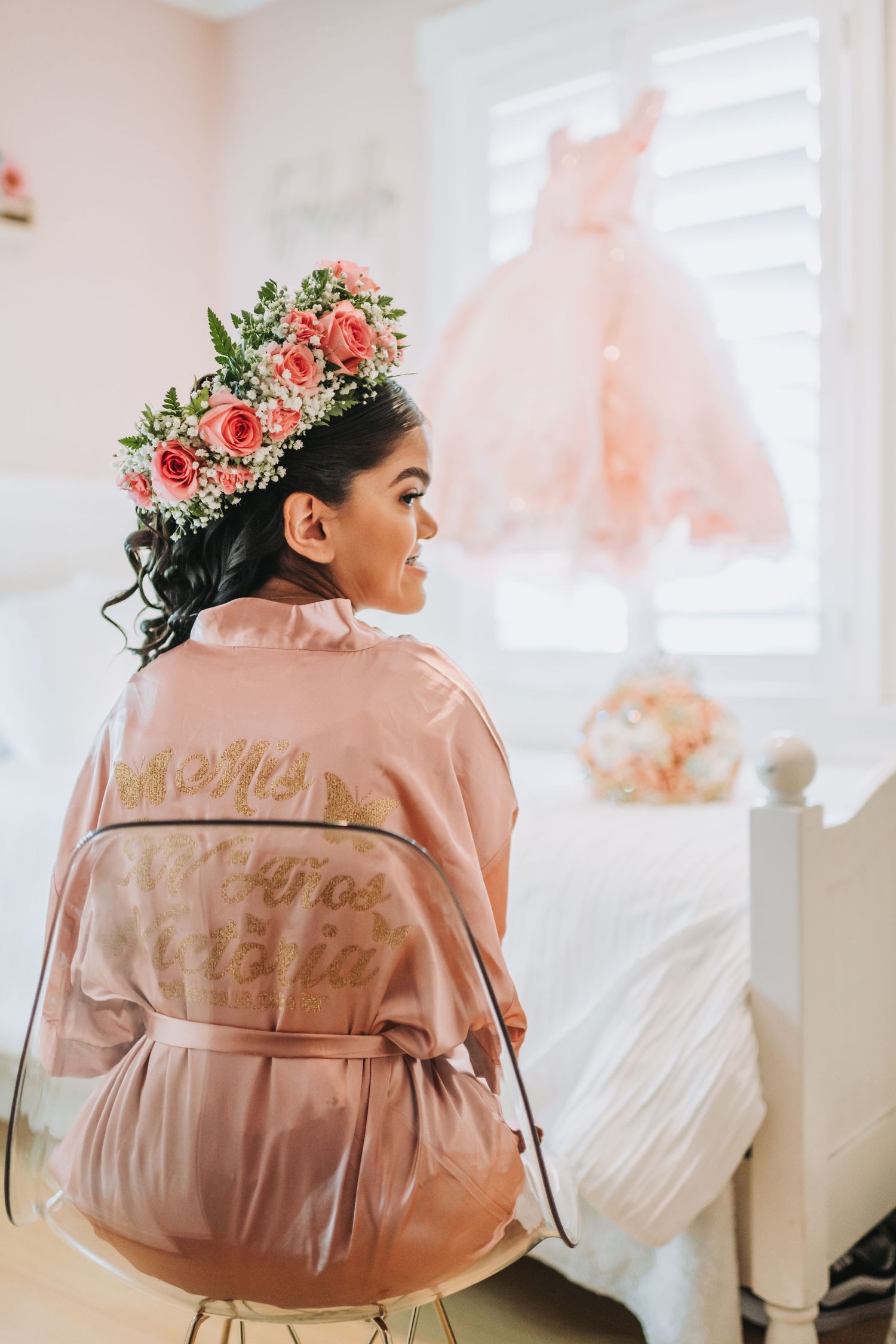 Getting ready photo showing a pink satin robe and floral crown with dress hanging in background.