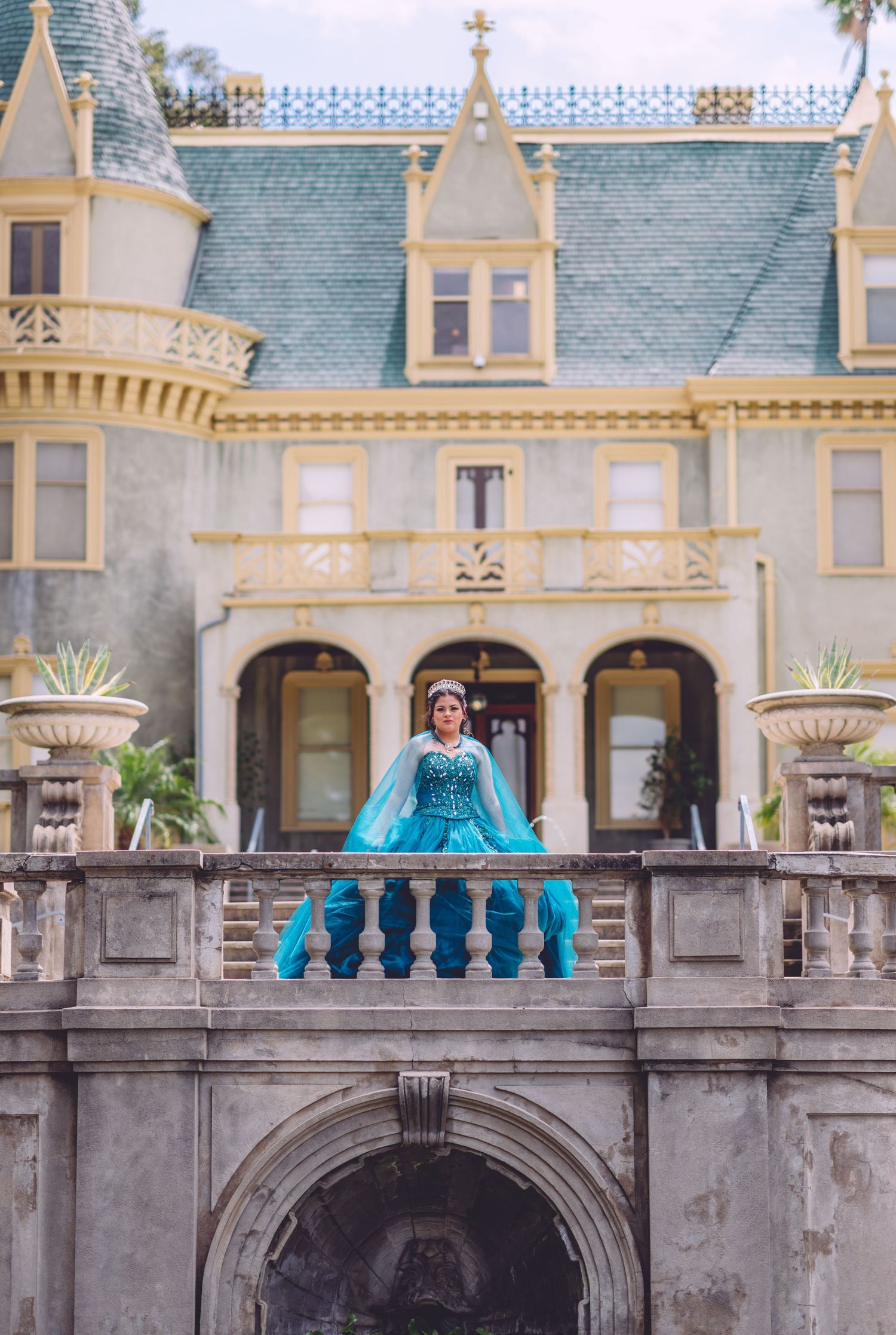 Turquoise ballgown creates fairytale moment on balcony of historic Victorian mansion.