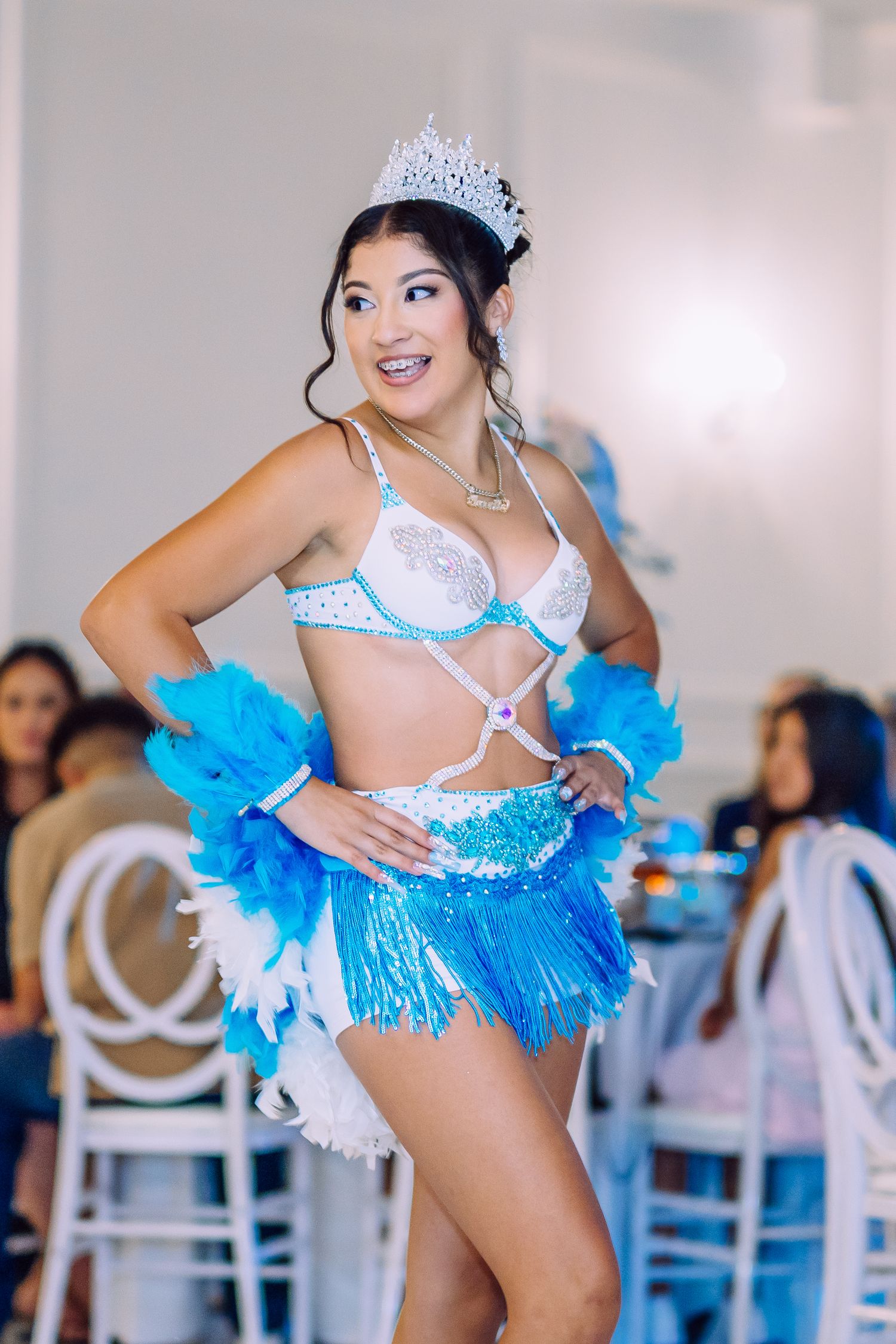 Performer in blue sequined costume with feathers and crown dancing at an event.