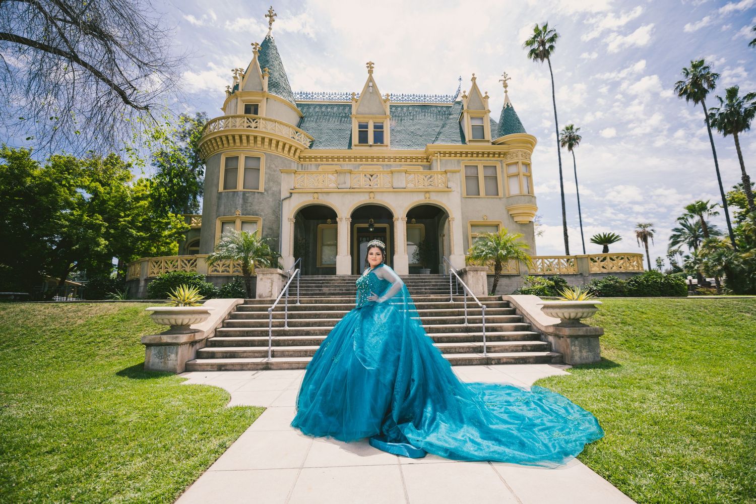 Dramatic turquoise ballgown with long train photographed in front of grand historic mansion.