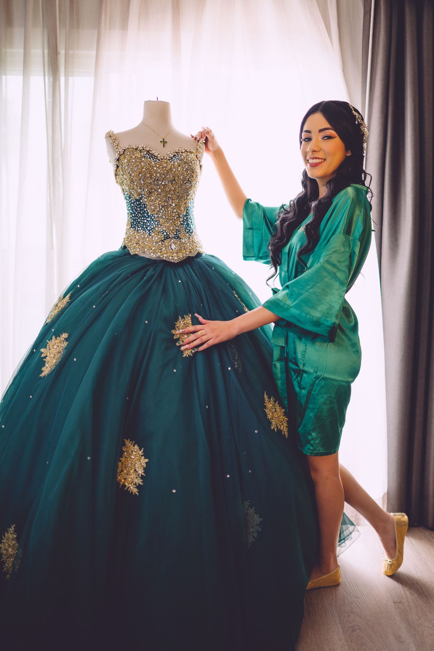 Beautiful emerald green ball gown with gold embellishments and crystals displayed on mannequin next to woman in matching robe.