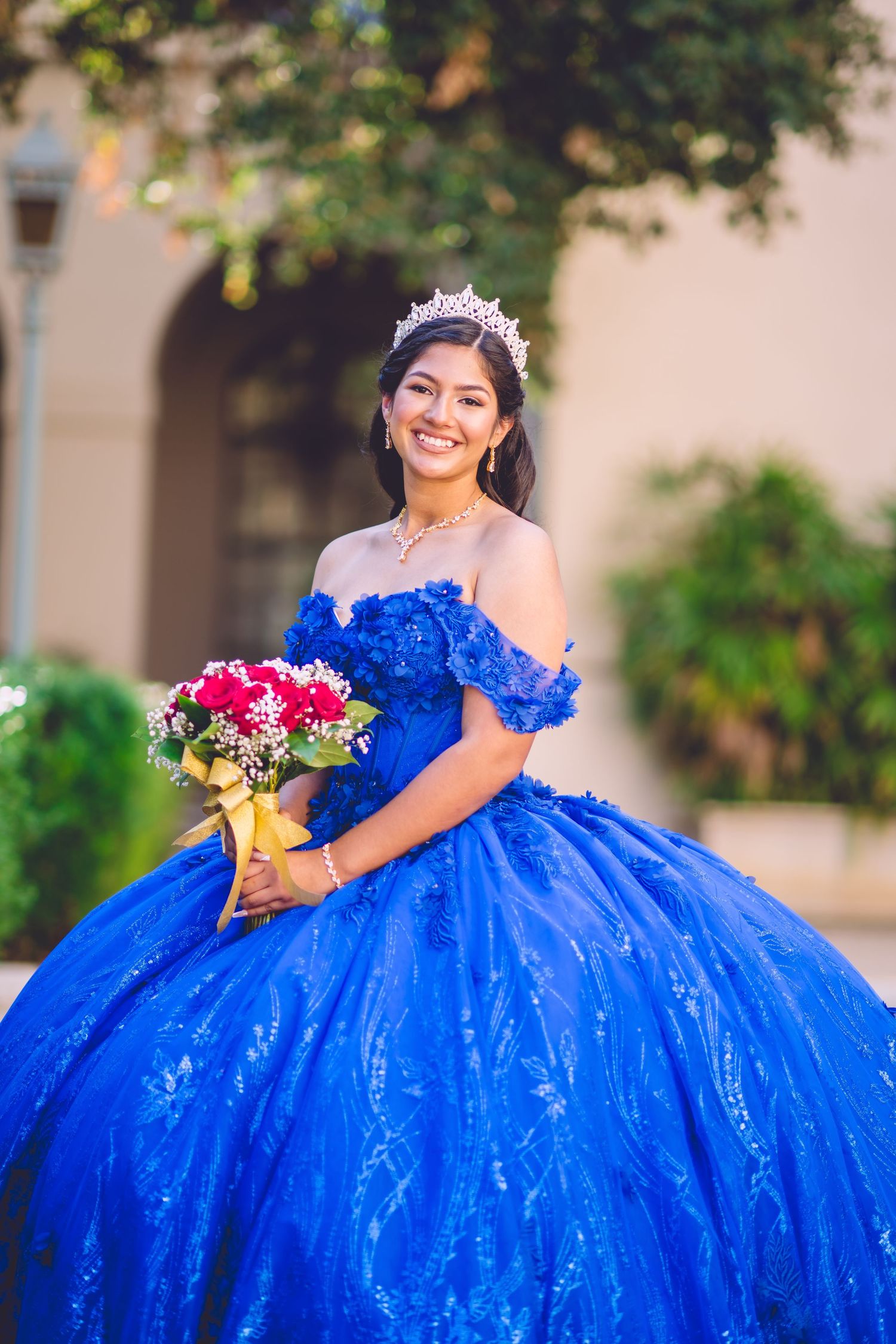 Stunning royal blue ballgown quinceañera dress sparkles in outdoor garden setting.