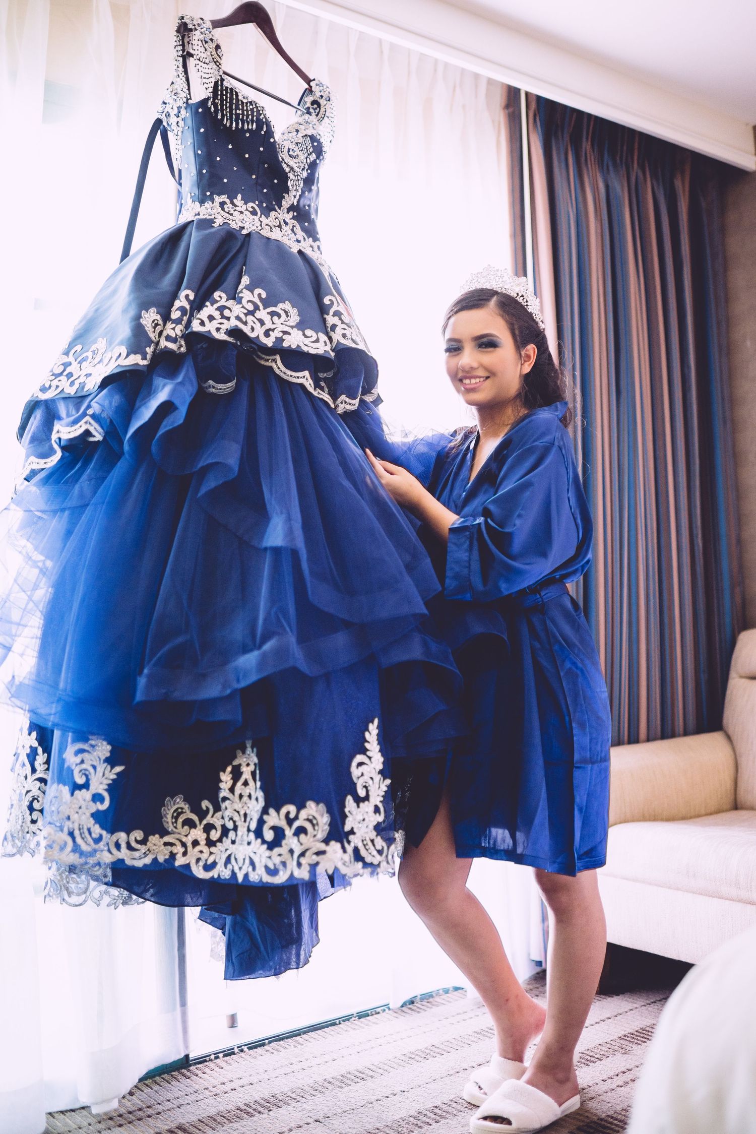 A stunning royal blue ball gown with white lace details hangs on display while someone in a blue robe admires it.