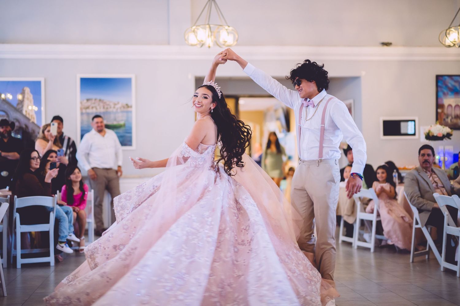 A couple dancing in an elegant ballroom with guests watching from their seats.