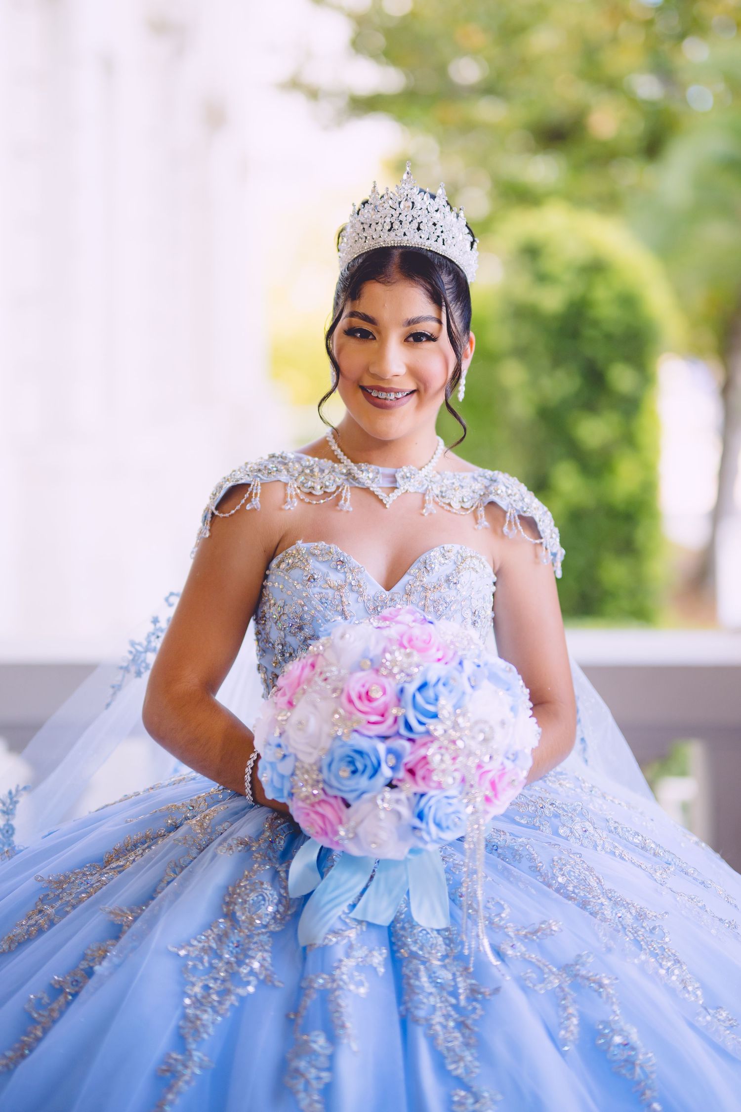 A quinceañera celebrates in a sparkling light blue ball gown with crystal details and holds a pink and blue bouquet.