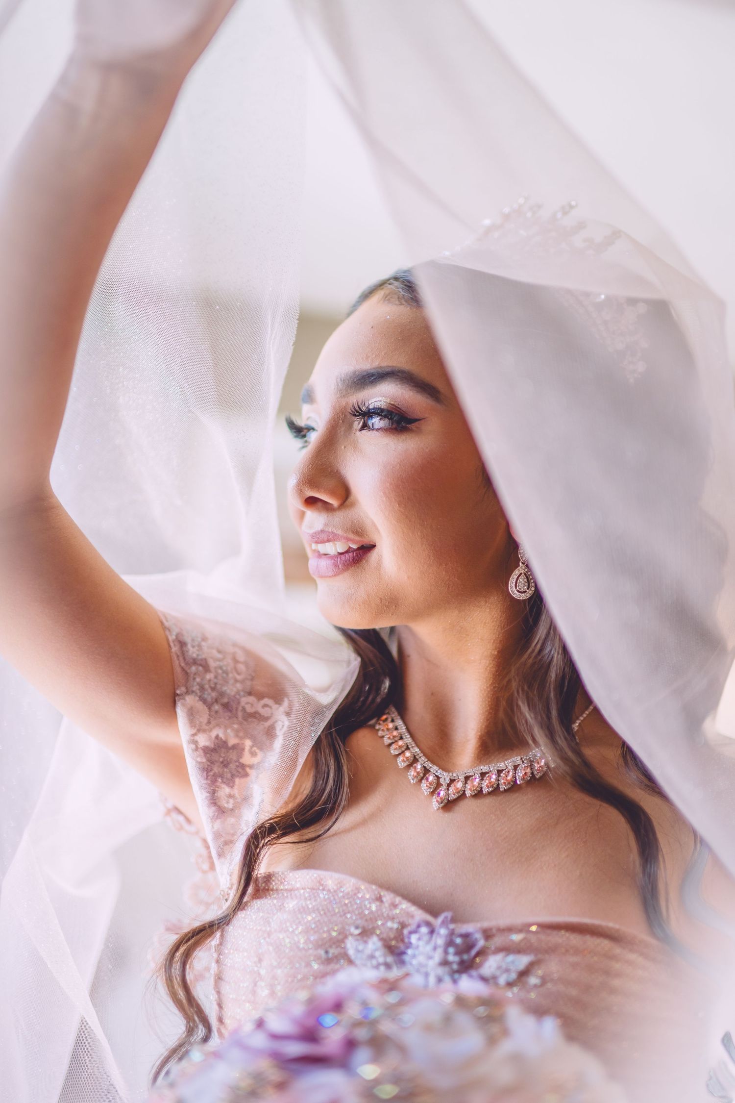 Bride in white veil and lace dress with crystal necklace smiles radiantly during wedding day portrait.