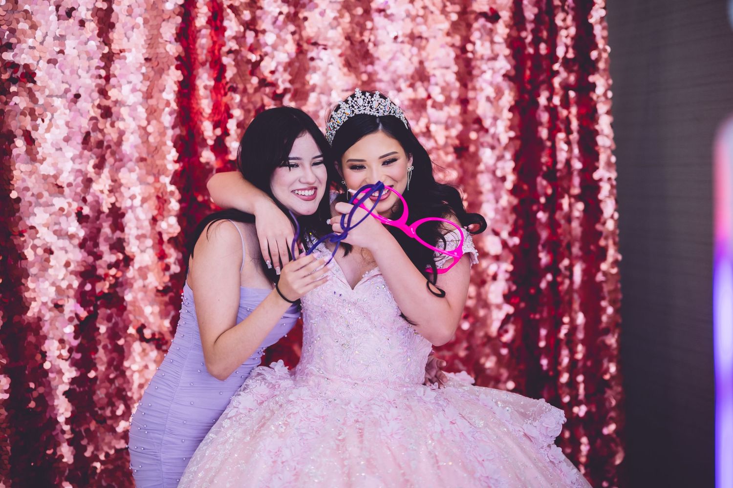 Celebration moment against sparkly pink backdrop with formal gowns and tiaras.
