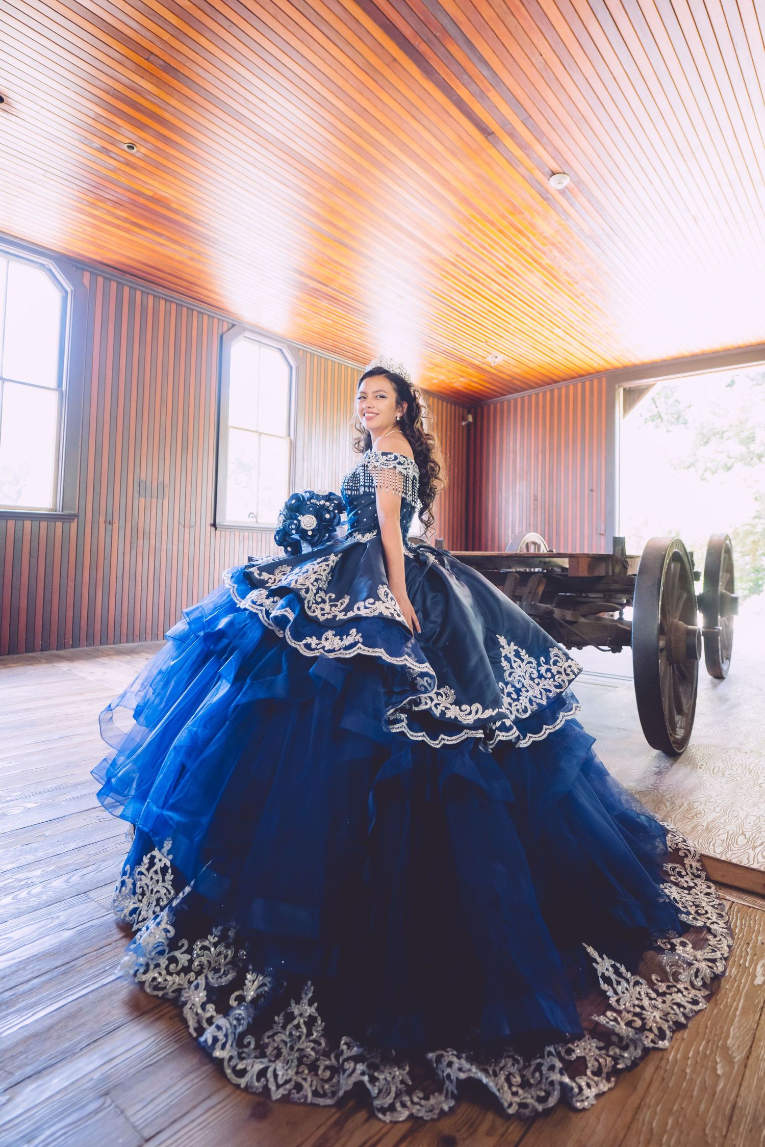 A stunning royal blue quinceañera dress with silver embellishments twirls elegantly on a wooden floor.