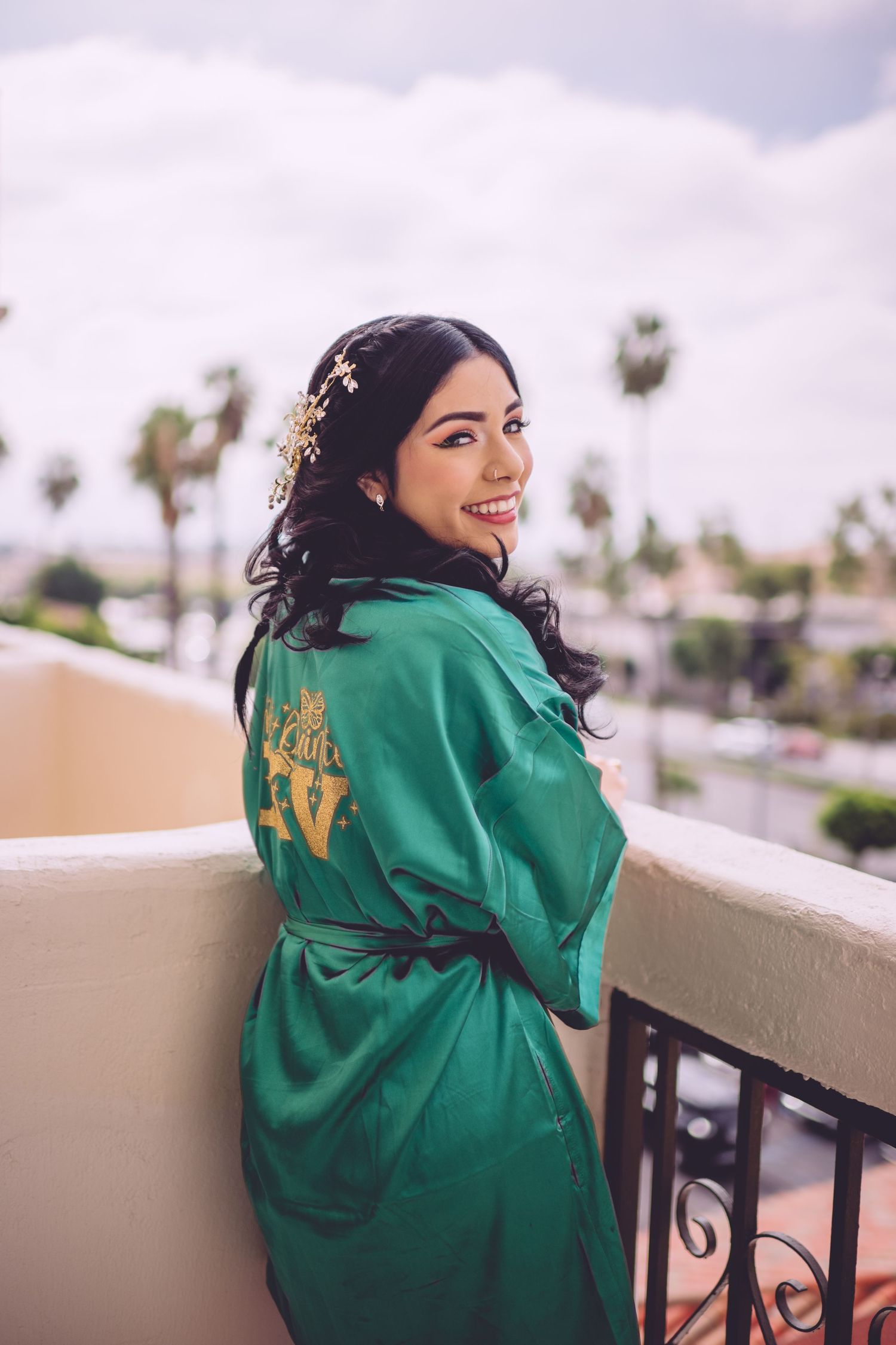 Joyful pre-wedding moment captured in an emerald green silk robe on a balcony with palm trees.