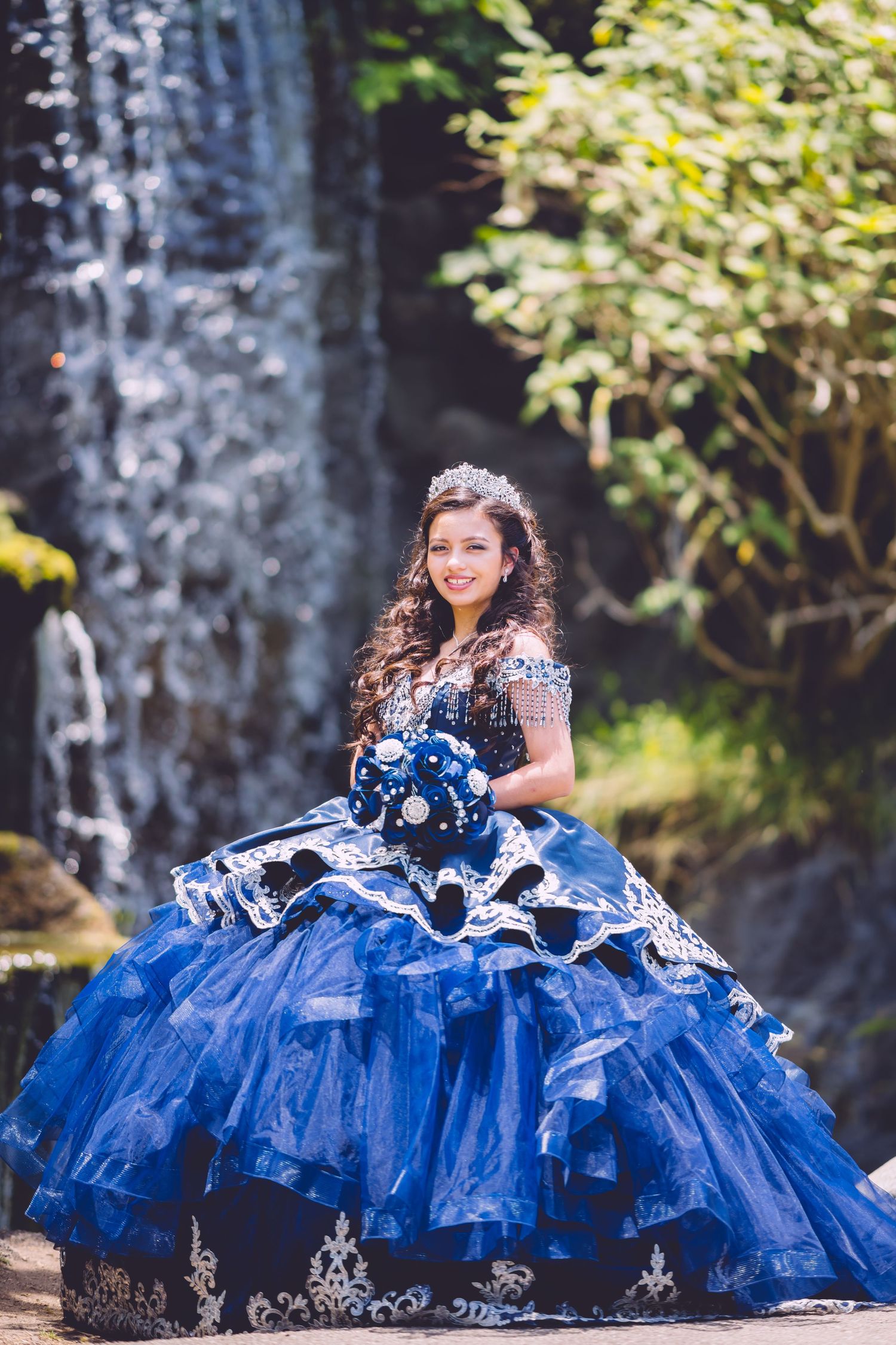 A royal blue quinceañera dress with white lace trim is photographed in multiple angles outdoors against a stone wall.