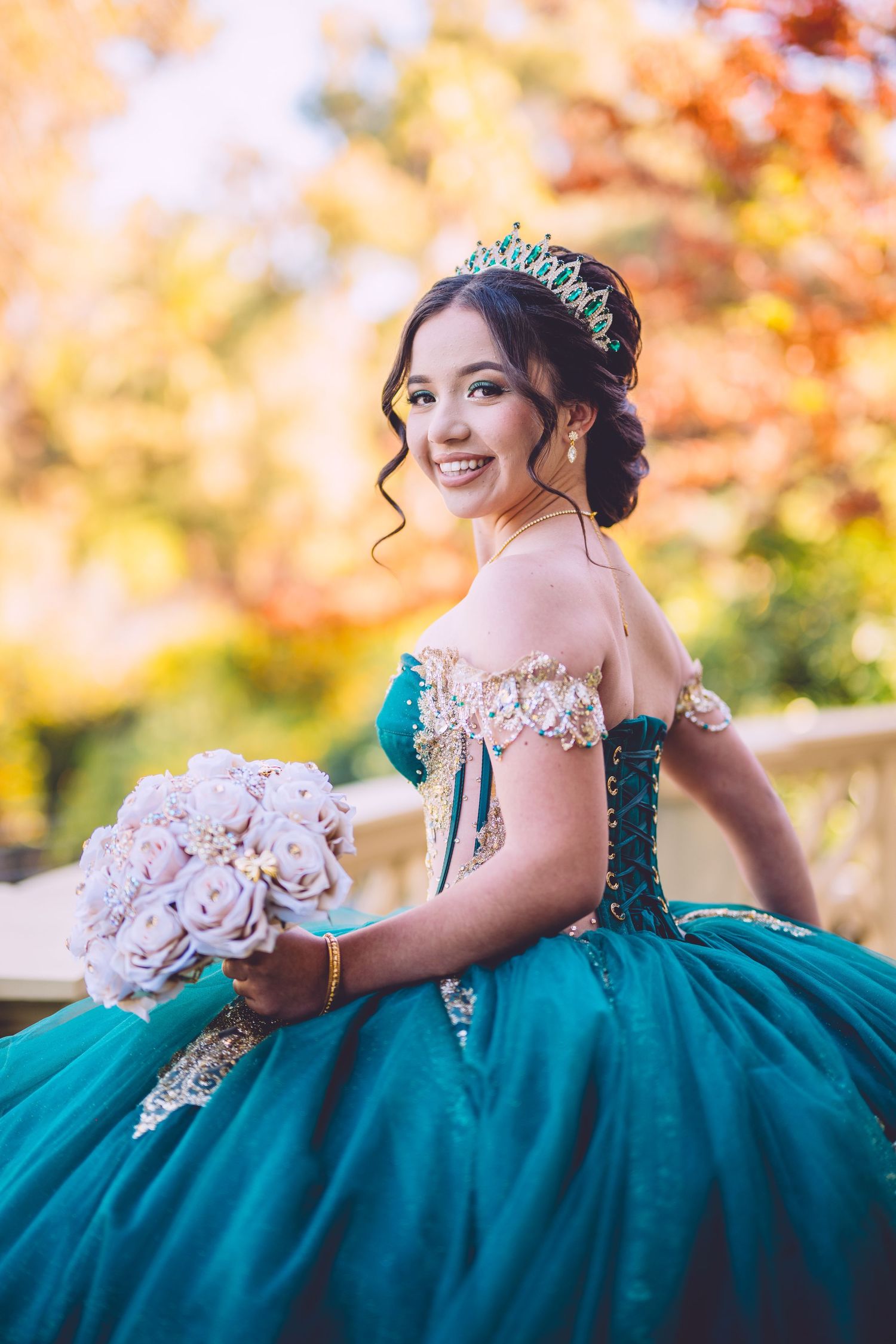 Elegant emerald green ballgown with off-shoulder design photographed against autumn foliage.