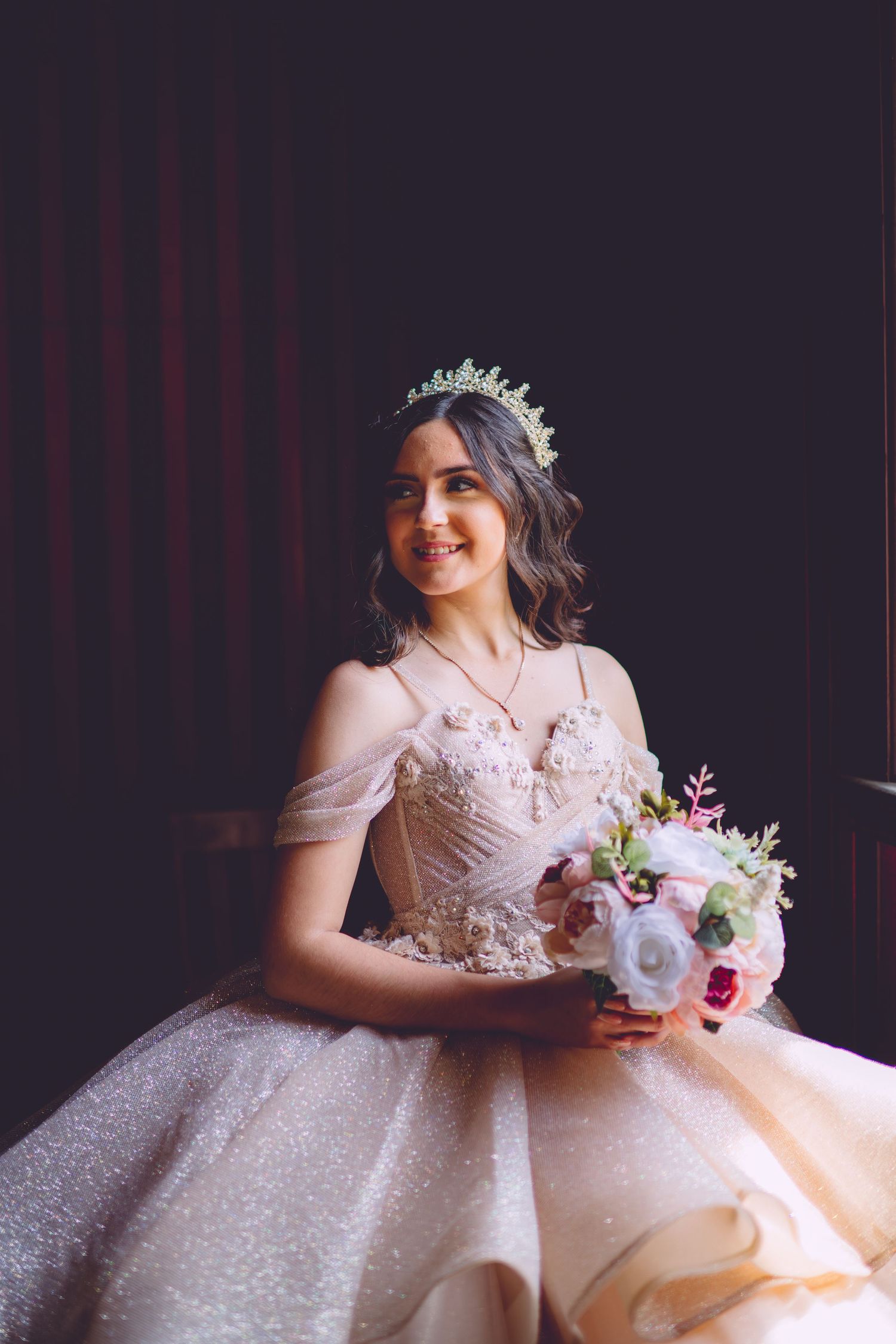 A stunning bridal portrait featuring a sparkly ball gown, delicate floral bouquet and crystal crown against a dark backdrop.