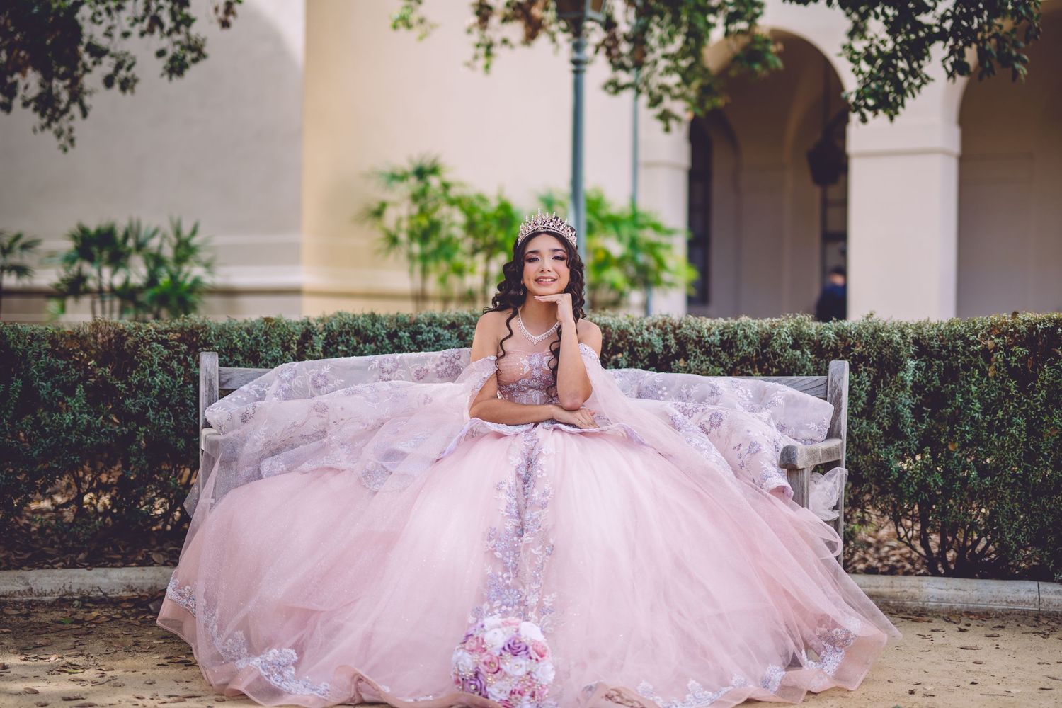 Dreamy pink quinceañera dress with floral appliques in elegant garden setting.