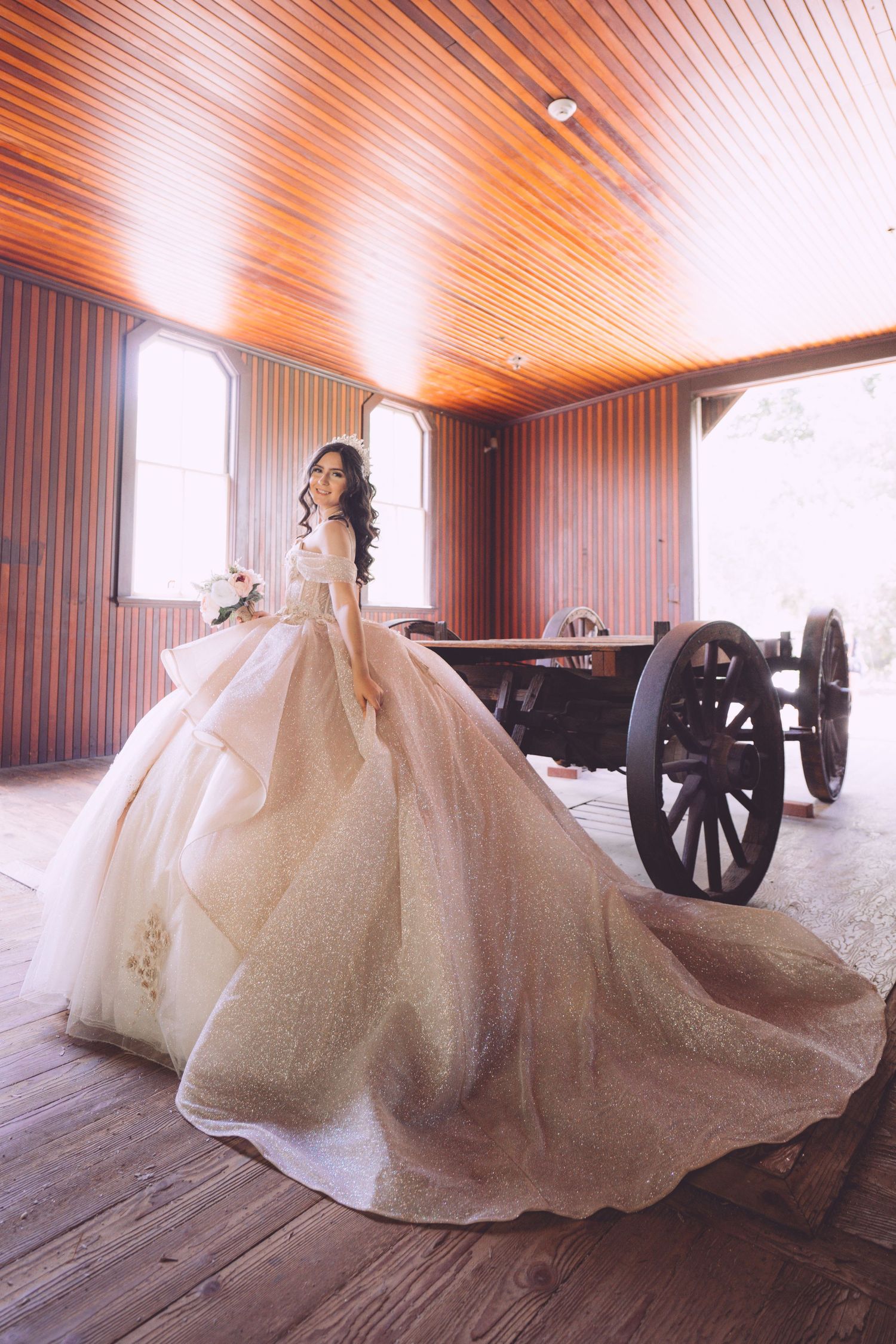 Majestic white wedding ball gown with long train in rustic wooden room with antique cannon.