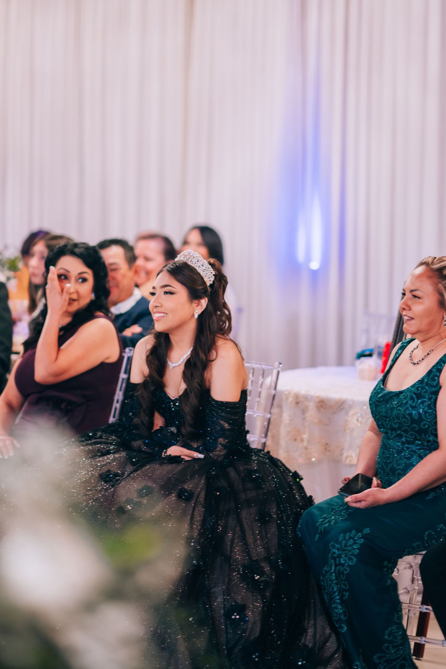Wedding guests in formal attire including elegant black and teal gowns seated during an evening reception.