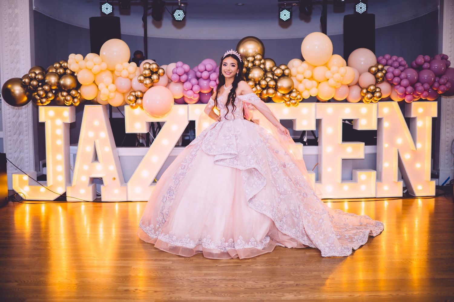 An elegant ballroom setup with lit-up letter decorations and peach and gold balloon arrangements.