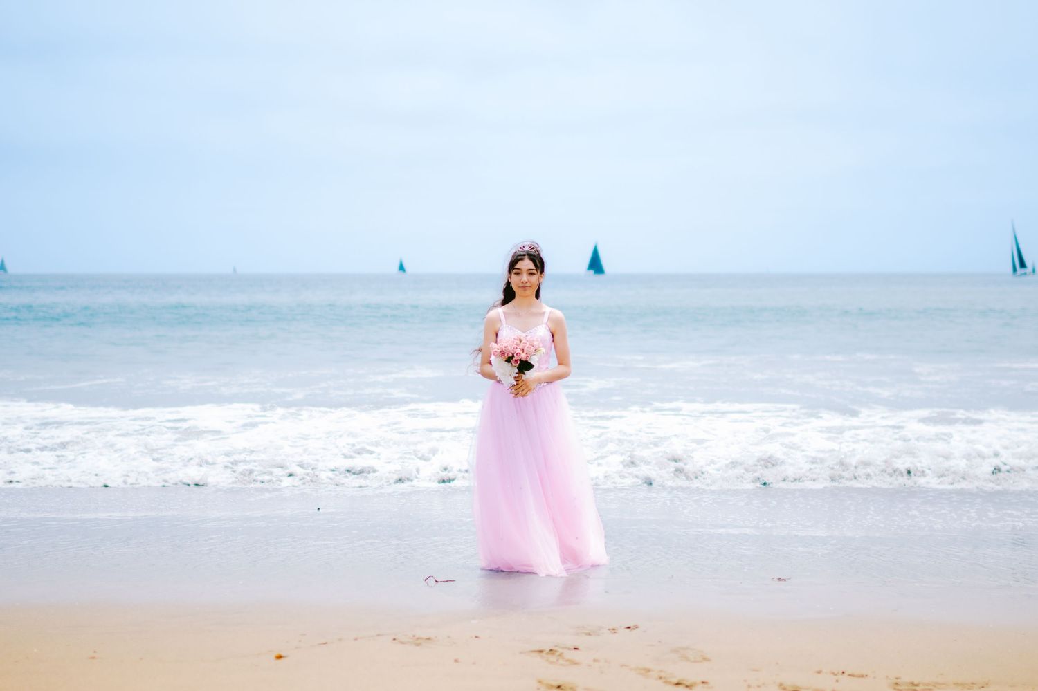 A person in a flowing pink dress walks gracefully along a serene beach shoreline at sunset.