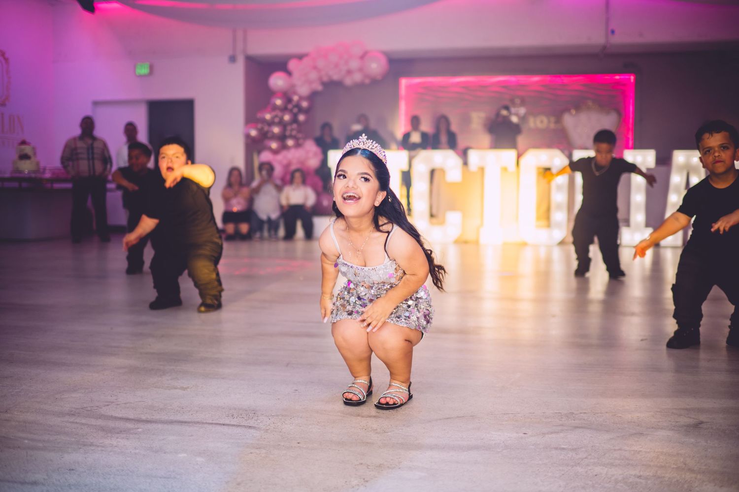 Dancing figure in sparkly dress under purple party lights.