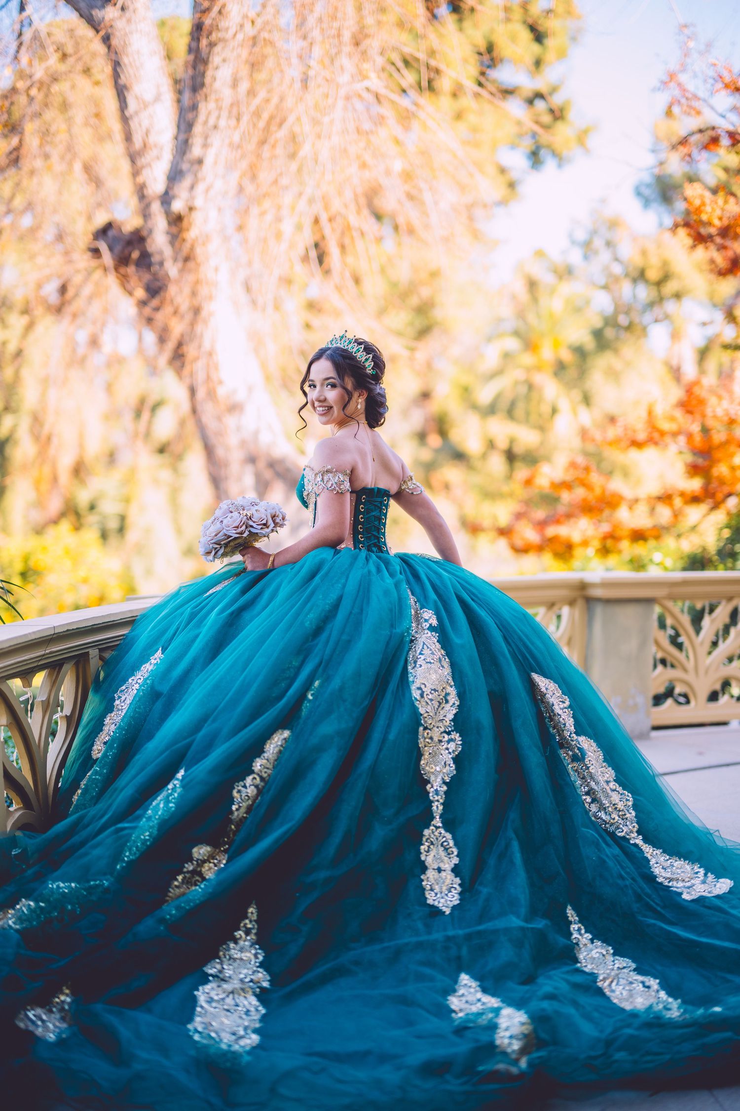 A teal blue quinceañera ball gown with white lace appliques photographed in a garden during golden hour.