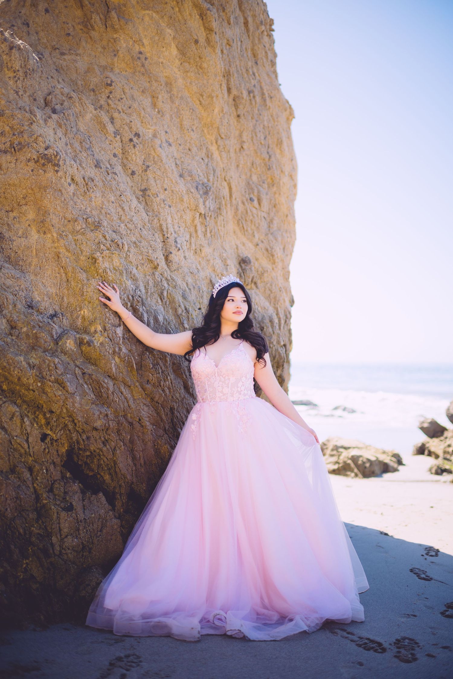 Romantic beach photoshoot featuring a flowing pink tulle gown next to dramatic oceanside cliffs.