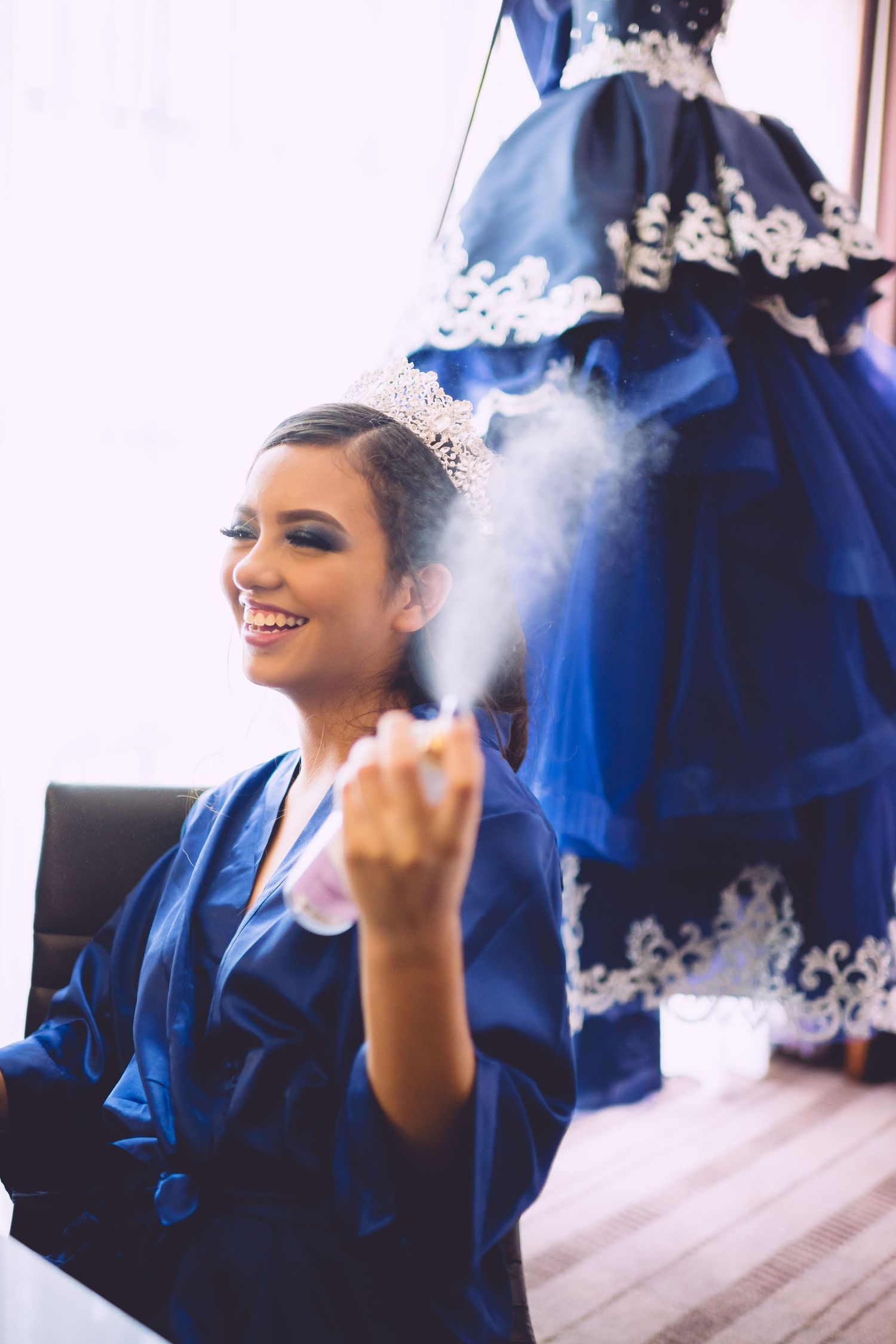 A blue ballgown dress with white lace trim hangs in the background as preparations take place.