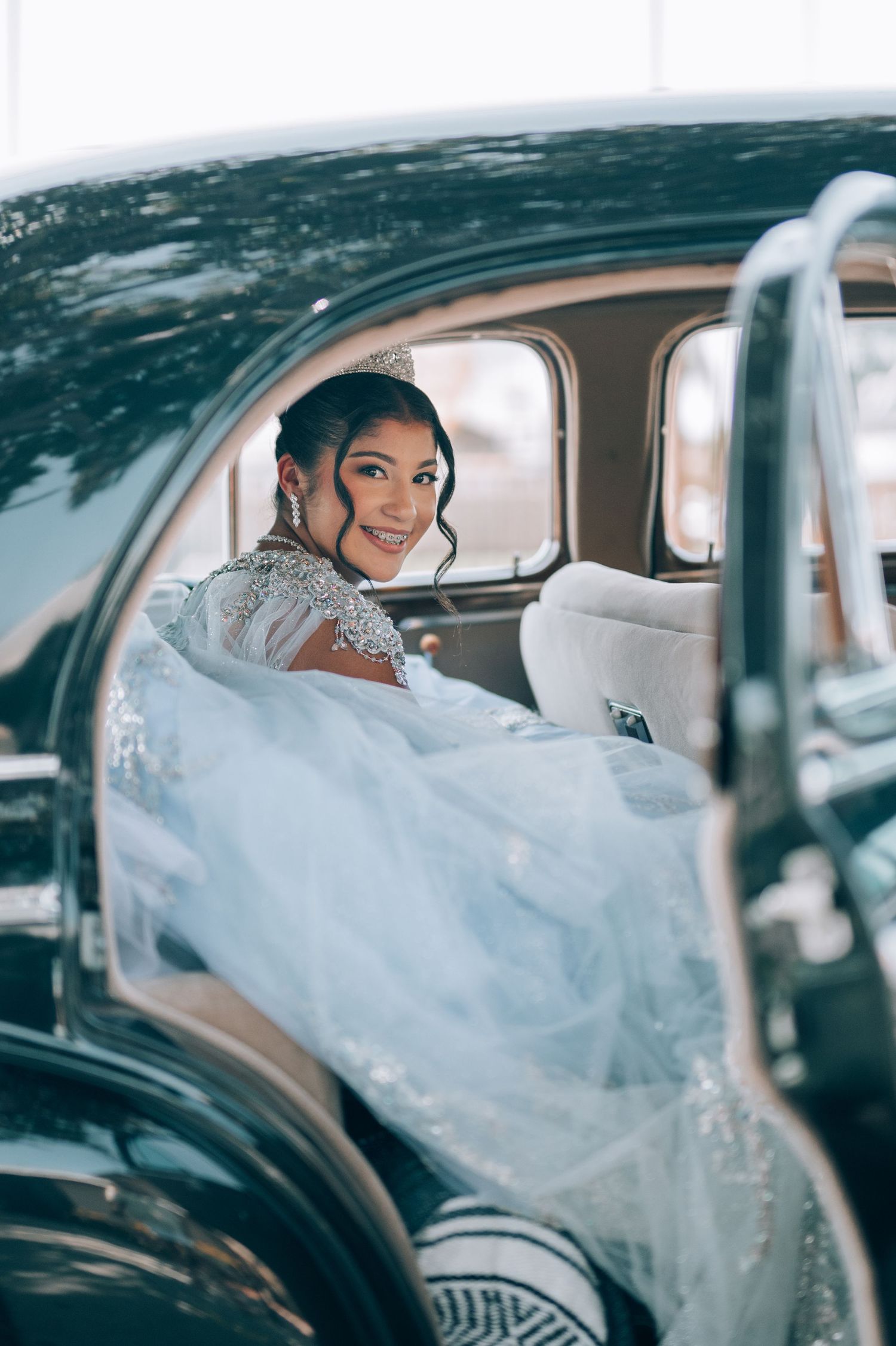 A stunning white lace wedding gown flows gracefully in the backseat of a classic black vintage car.