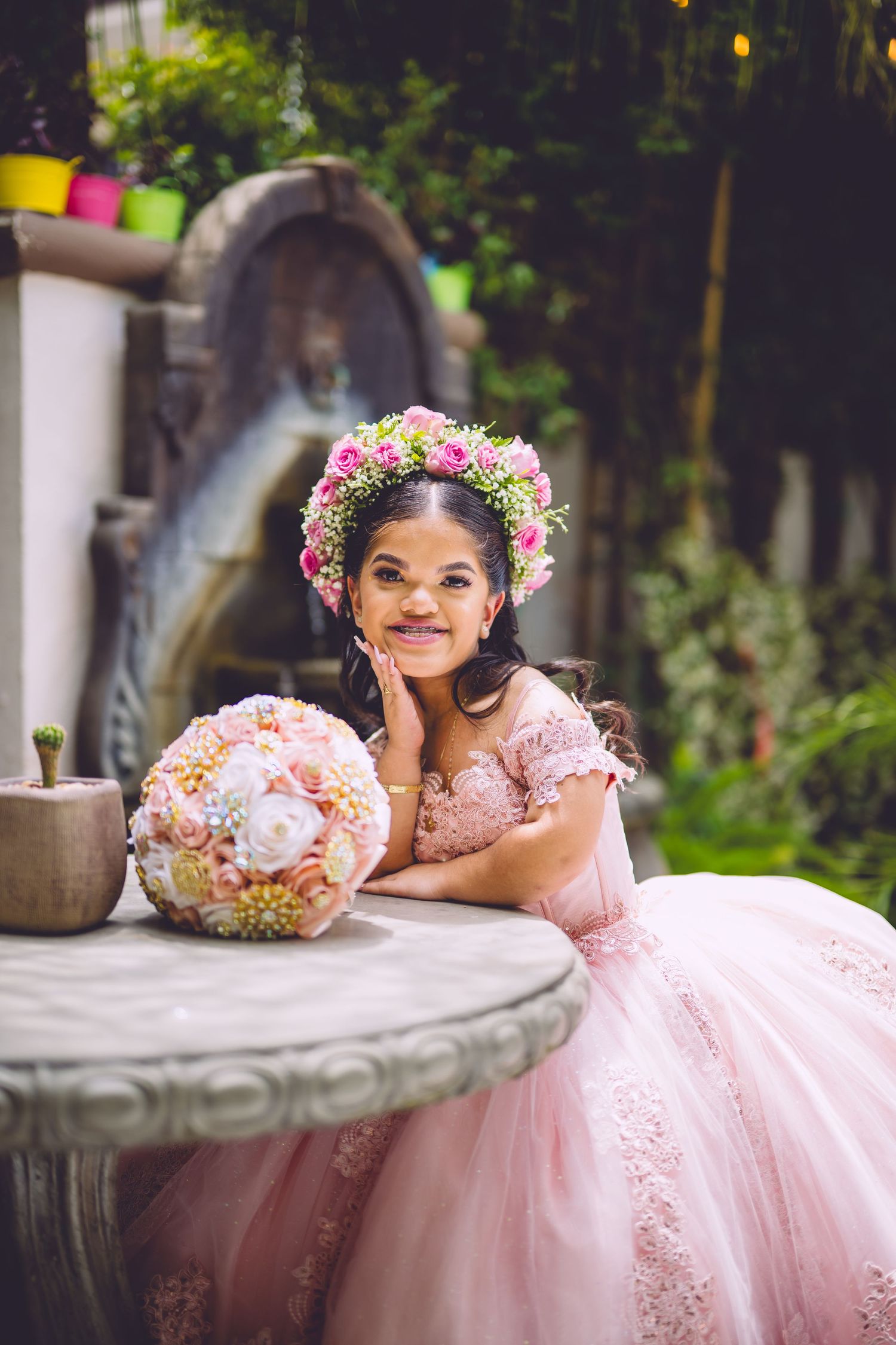 A pink ballgown and floral crown create a magical scene by garden fountain.
