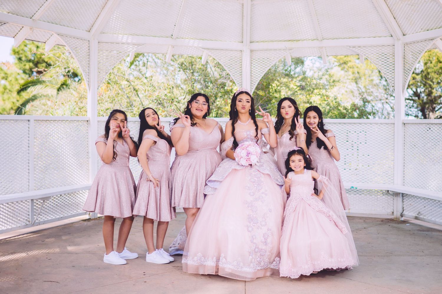 A celebration group photo featuring matching pink dresses in an elegant white gazebo setting.