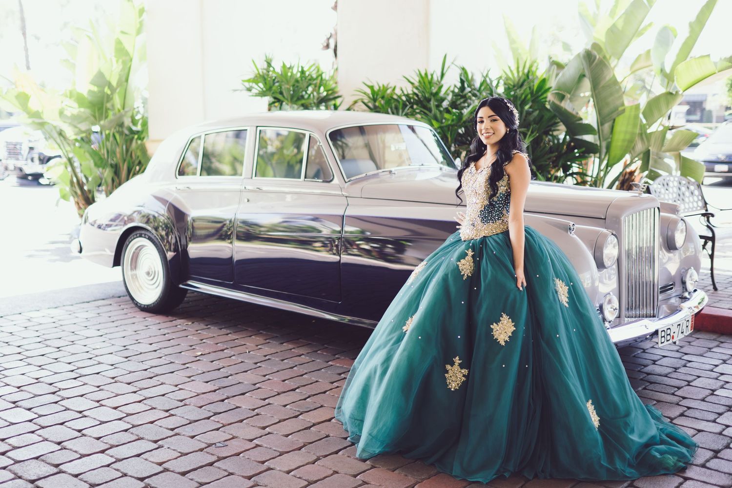 An emerald green ballgown poses elegantly next to a vintage Rolls Royce.