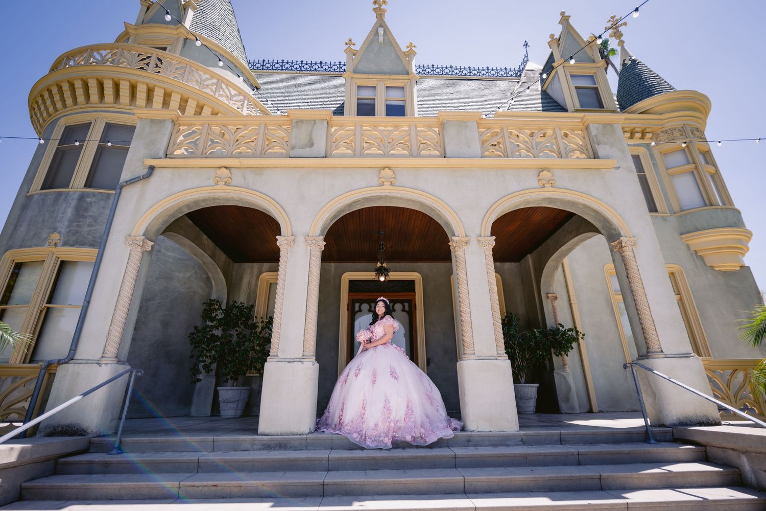 Elegant quinceanera photo session on the grand steps of a historic yellow and white Spanish colonial style building.