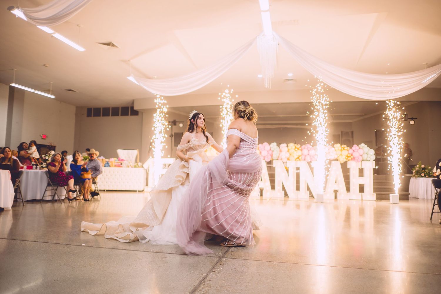A wedding celebration in a white decorated reception hall with sparklers and soft pink decor creating a romantic atmosphere.
