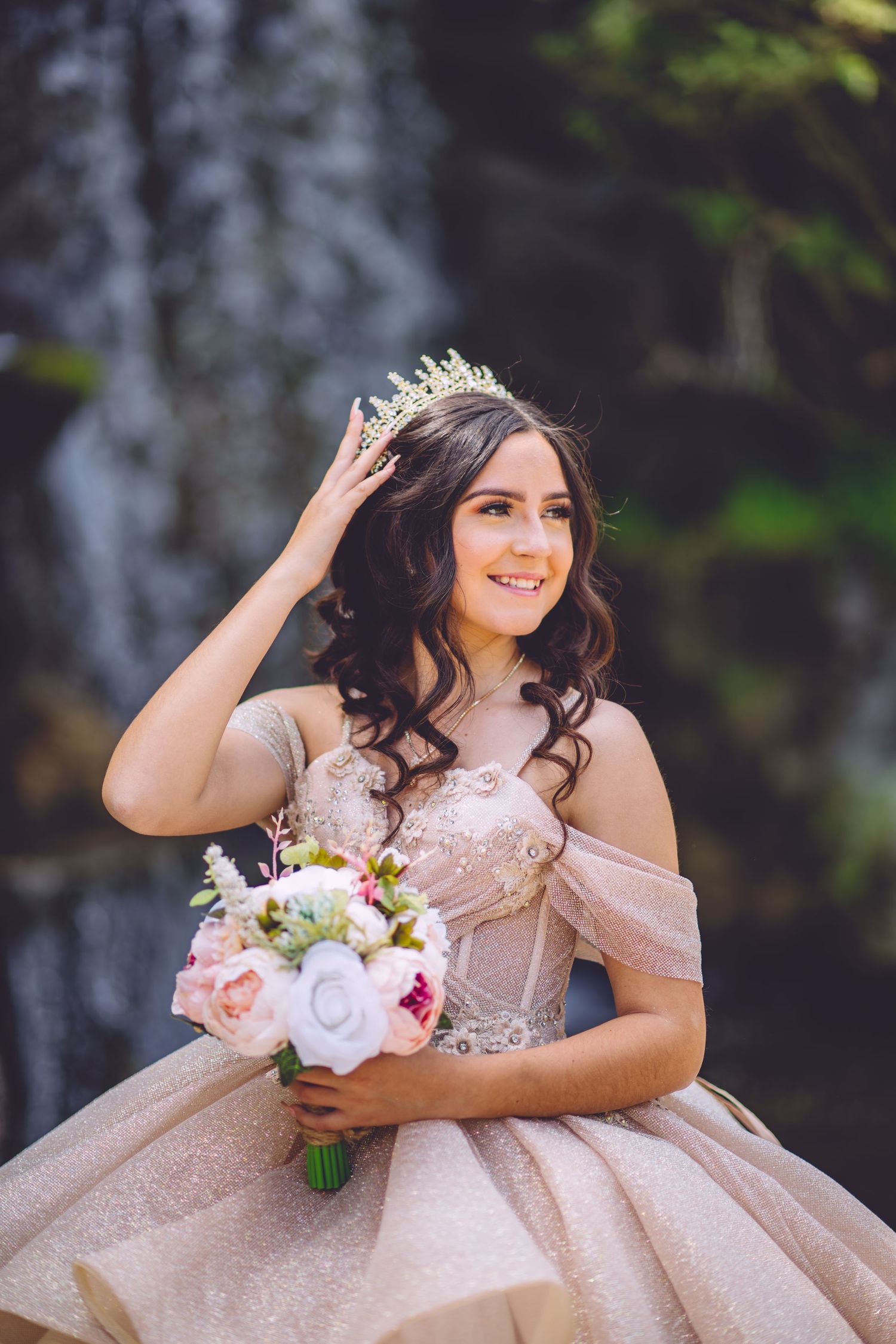 Dreamy bridal photo showcasing a blush ball gown and bouquet in front of a cascading waterfall.