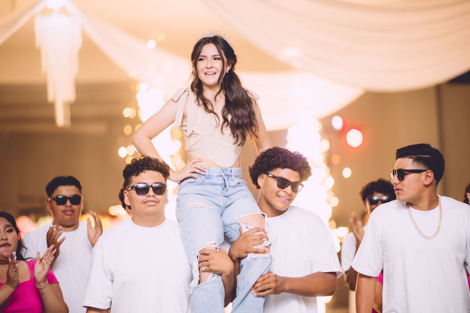 Group wearing white shirts supporting and lifting someone during celebration event with soft lighting decor.